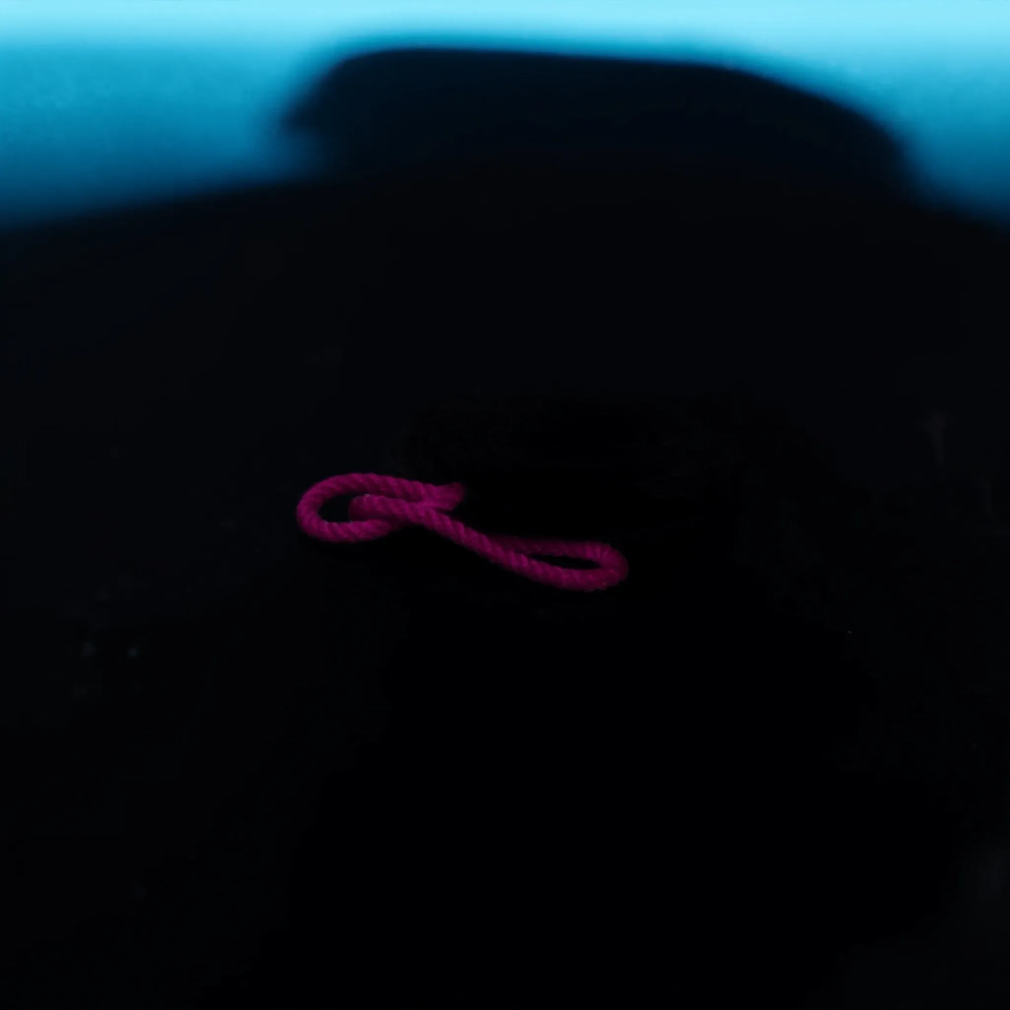A single coil of thick rope resting on dark slate, clearly visible, one pink strand woven through it, soft cyan rim light, nothing else in frame