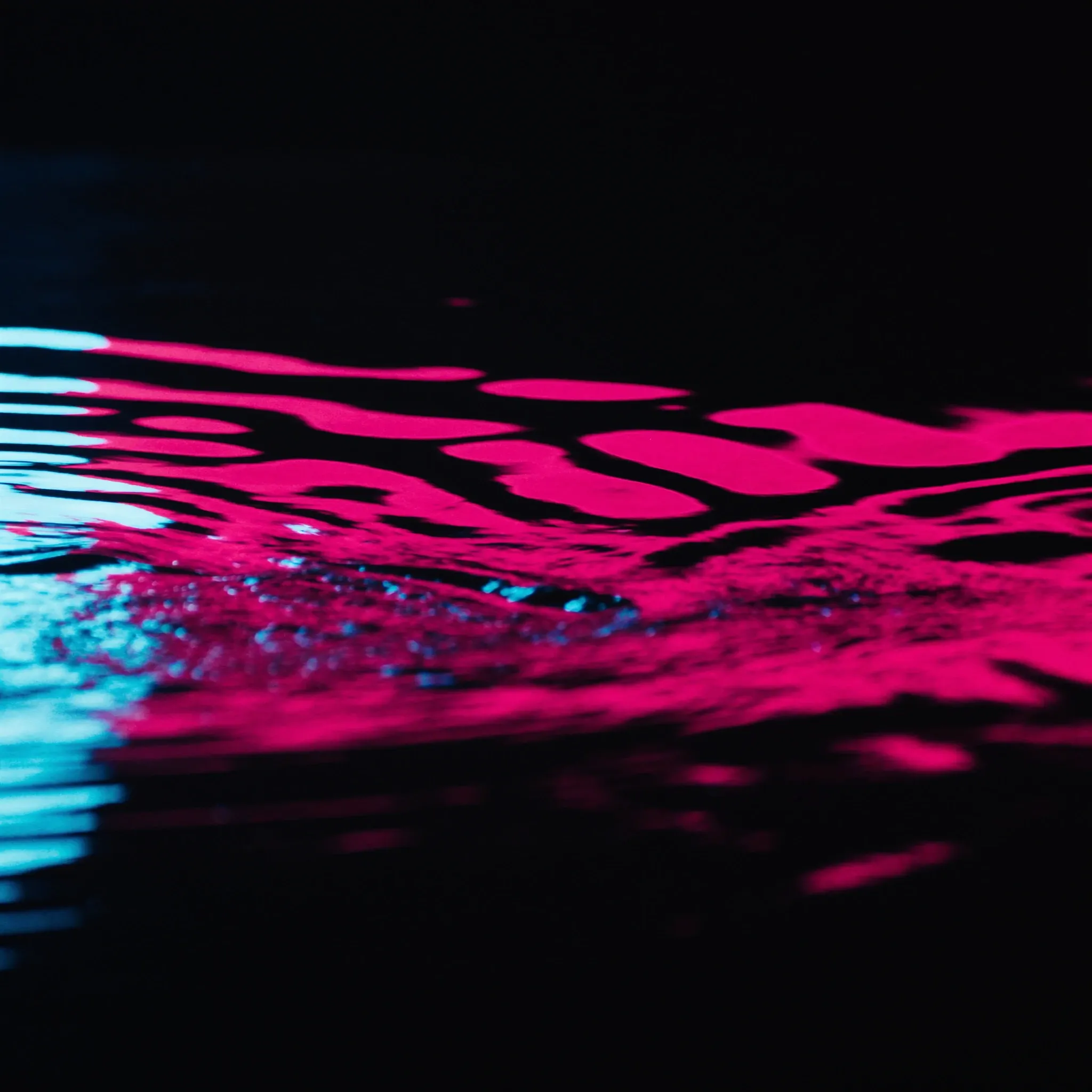 Smooth ripples spreading across a calm dark pool, pink and cyan reflections