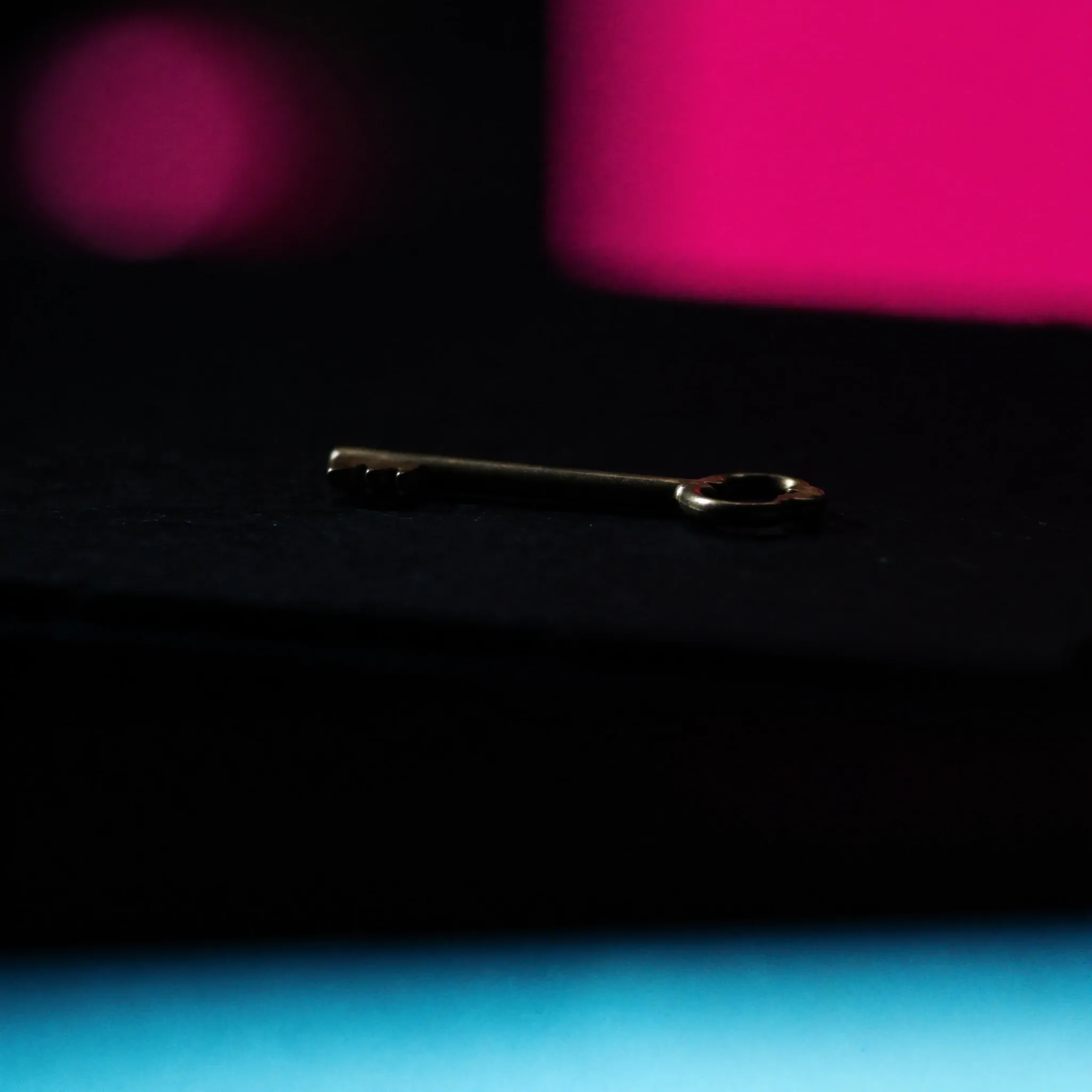 A heavy old brass key resting on dark slate, rim-lit in pink