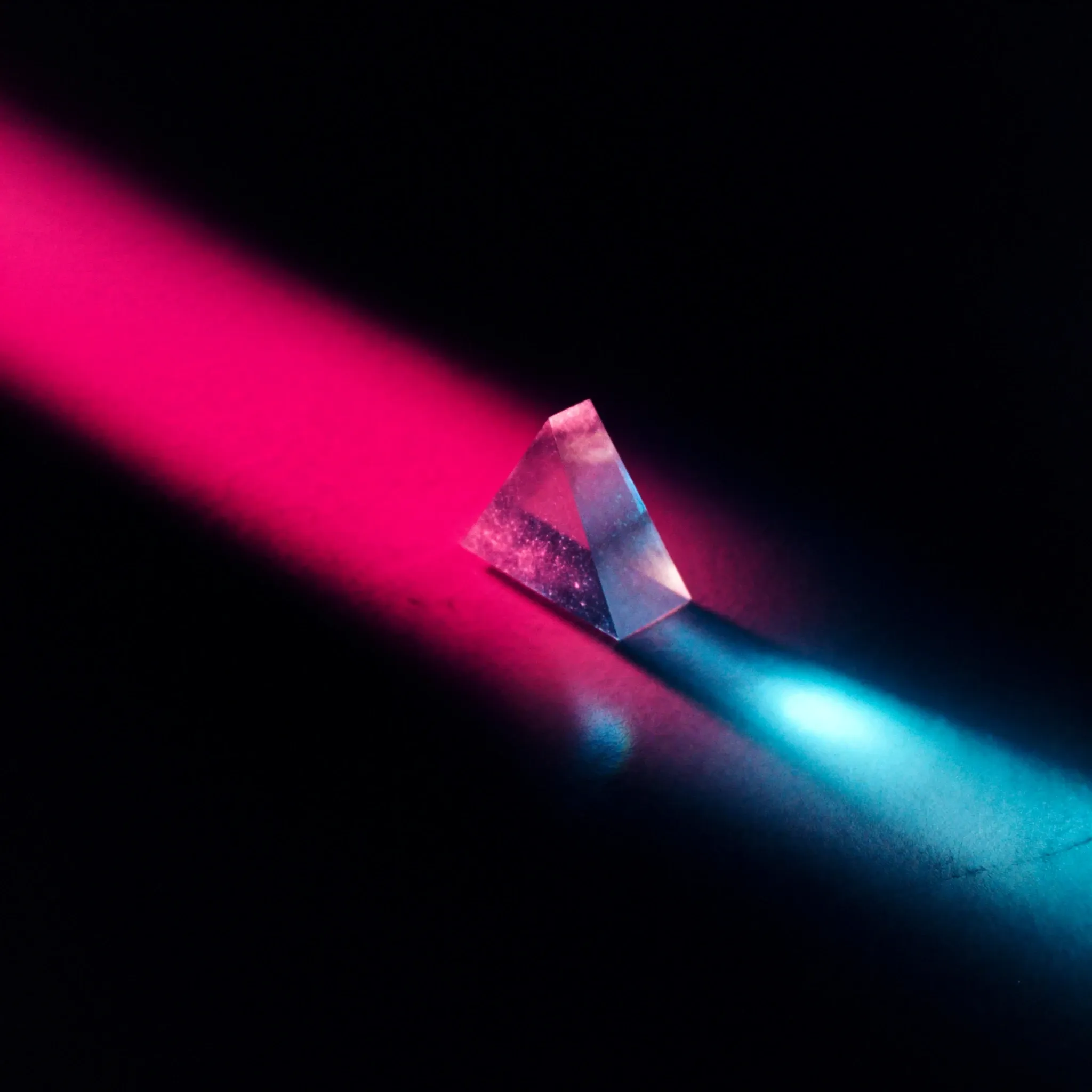 Light refracting through a glass prism into a clean band of pink, blue and cyan across a dark surface