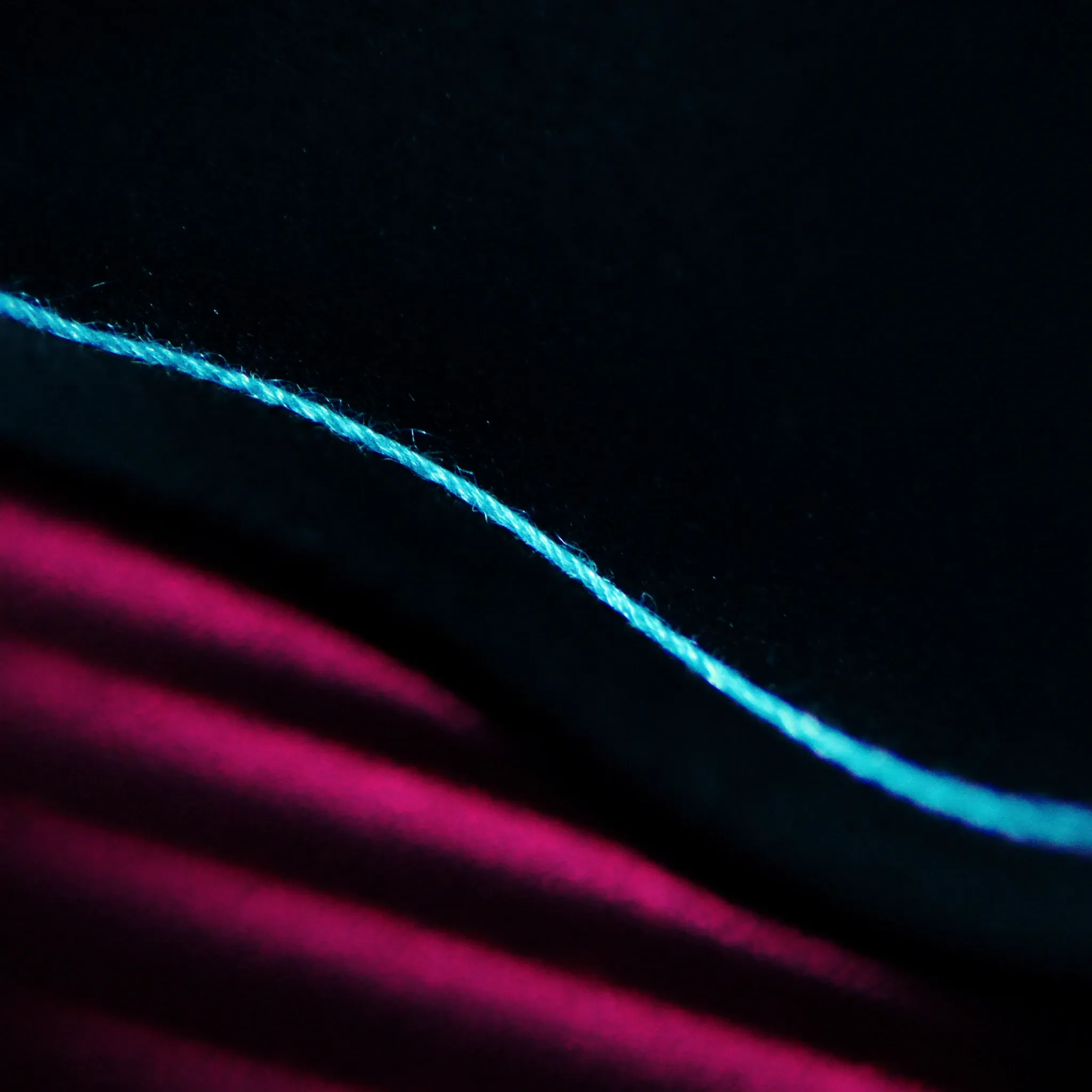 A single bright cyan thread stitched in a clean line through dark felt, macro