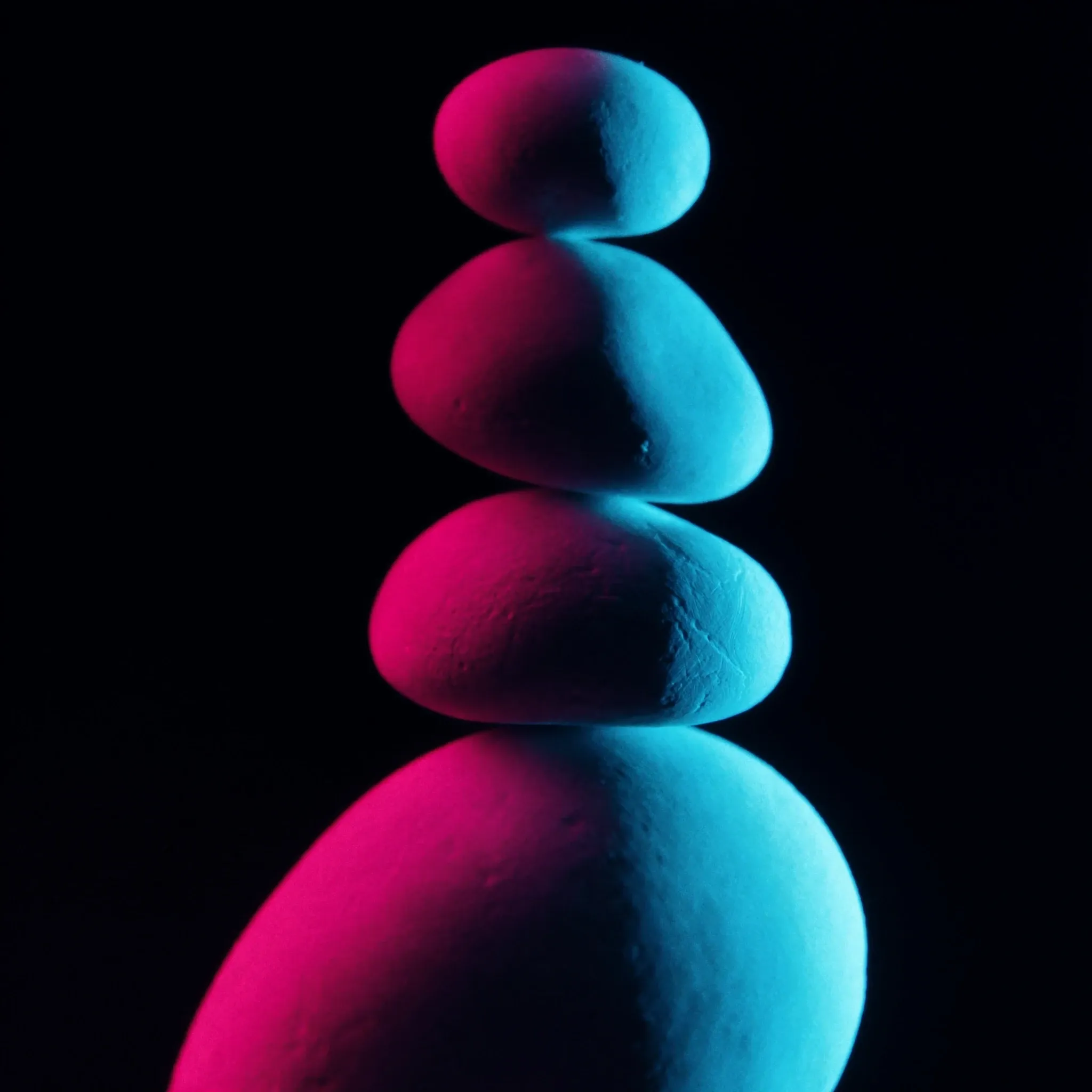 Smooth river stones of different sizes balanced in a clean vertical stack, lit cyan from one side against black
