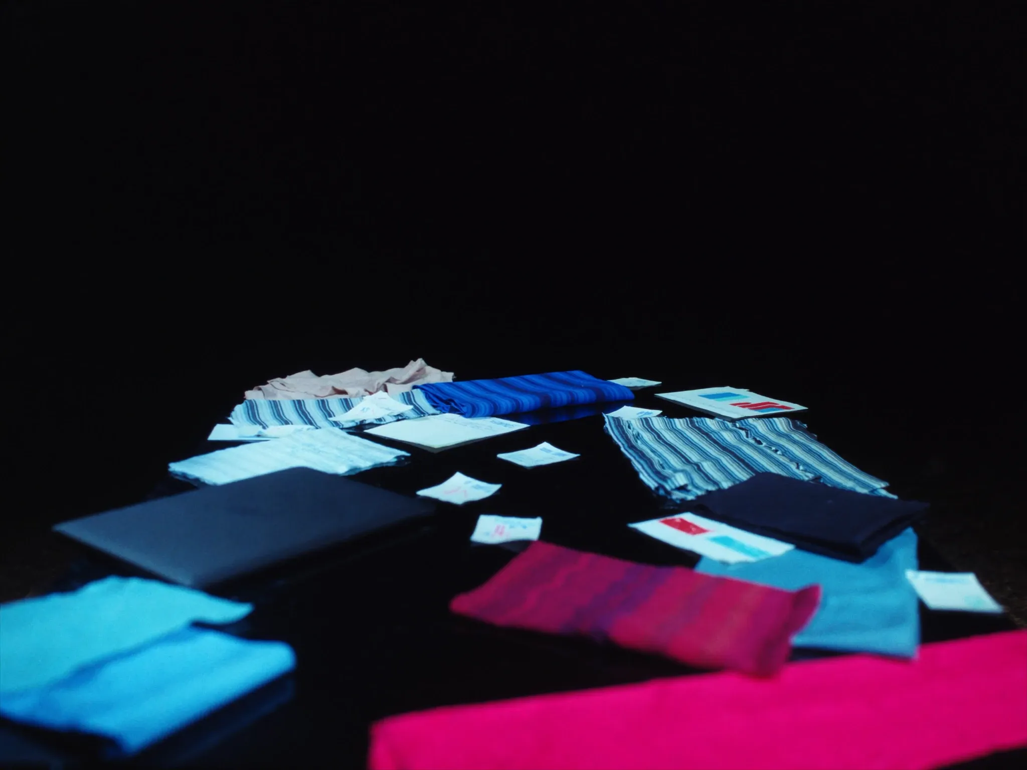 Mismatched fabric swatches in clashing colours and patterns scattered across a dark table, hard side light