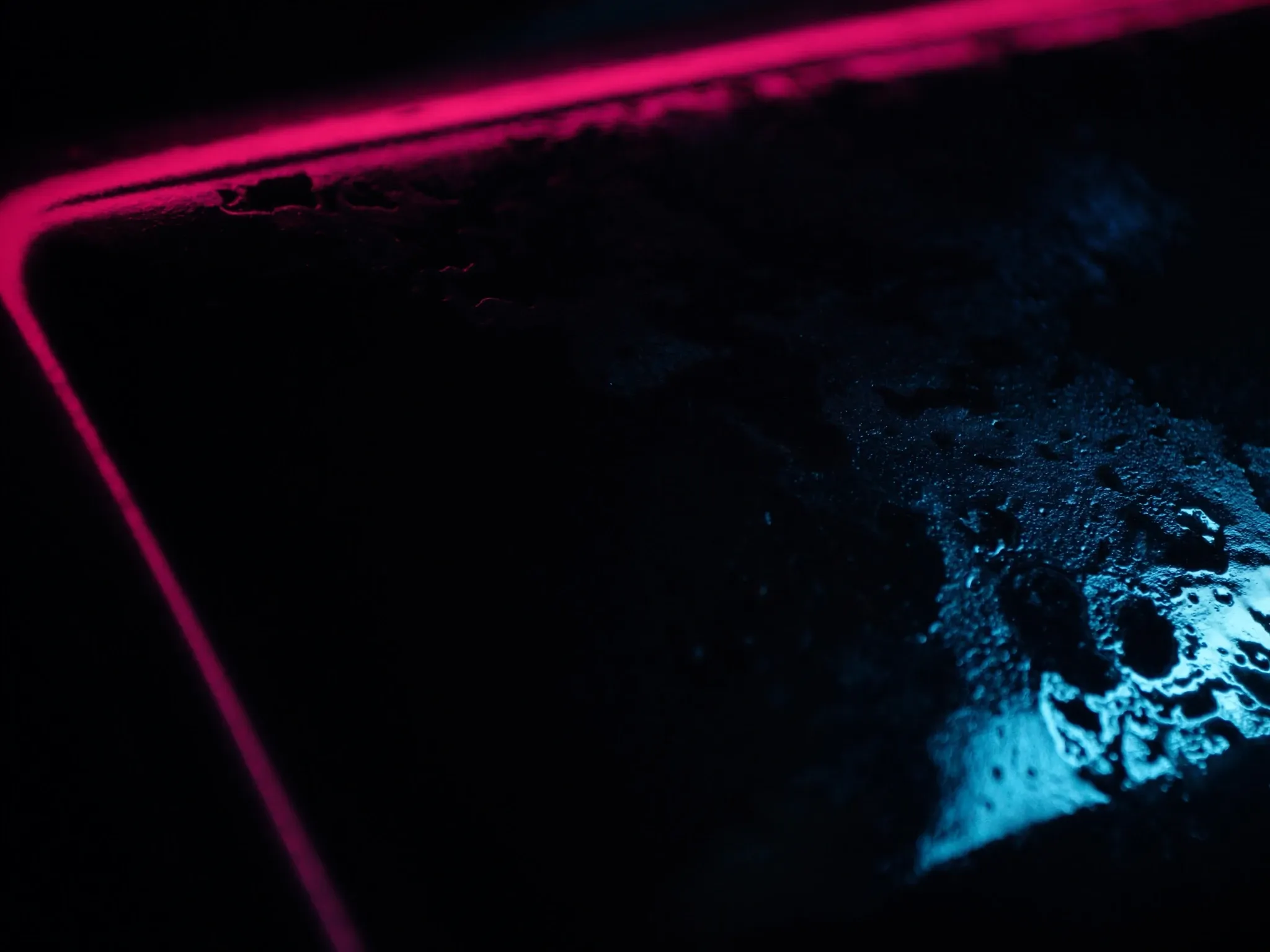 Rust spreading across a once-polished dark steel surface, macro, a thin pink rim light, nothing else in frame