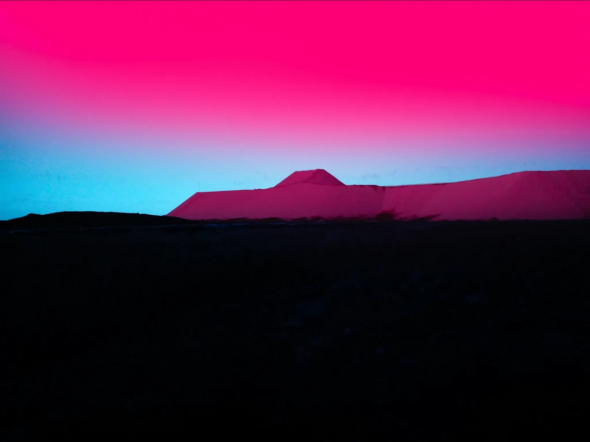 A flat-topped mine dump on the Johannesburg horizon at golden dusk, its pale sand slopes glowing pink and clearly visible, dry highveld grass in the foreground