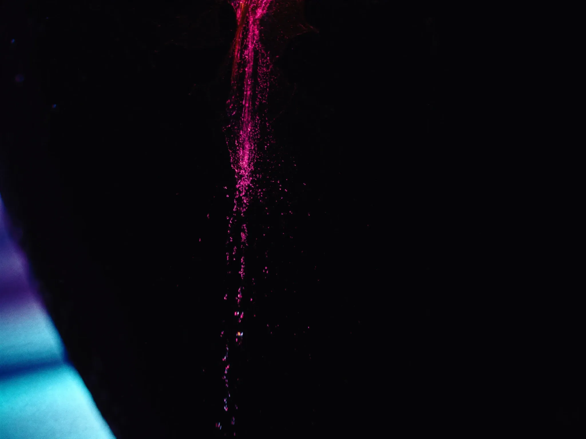 Water escaping through fine cracks in a dark vessel, droplets lit pink as they fall