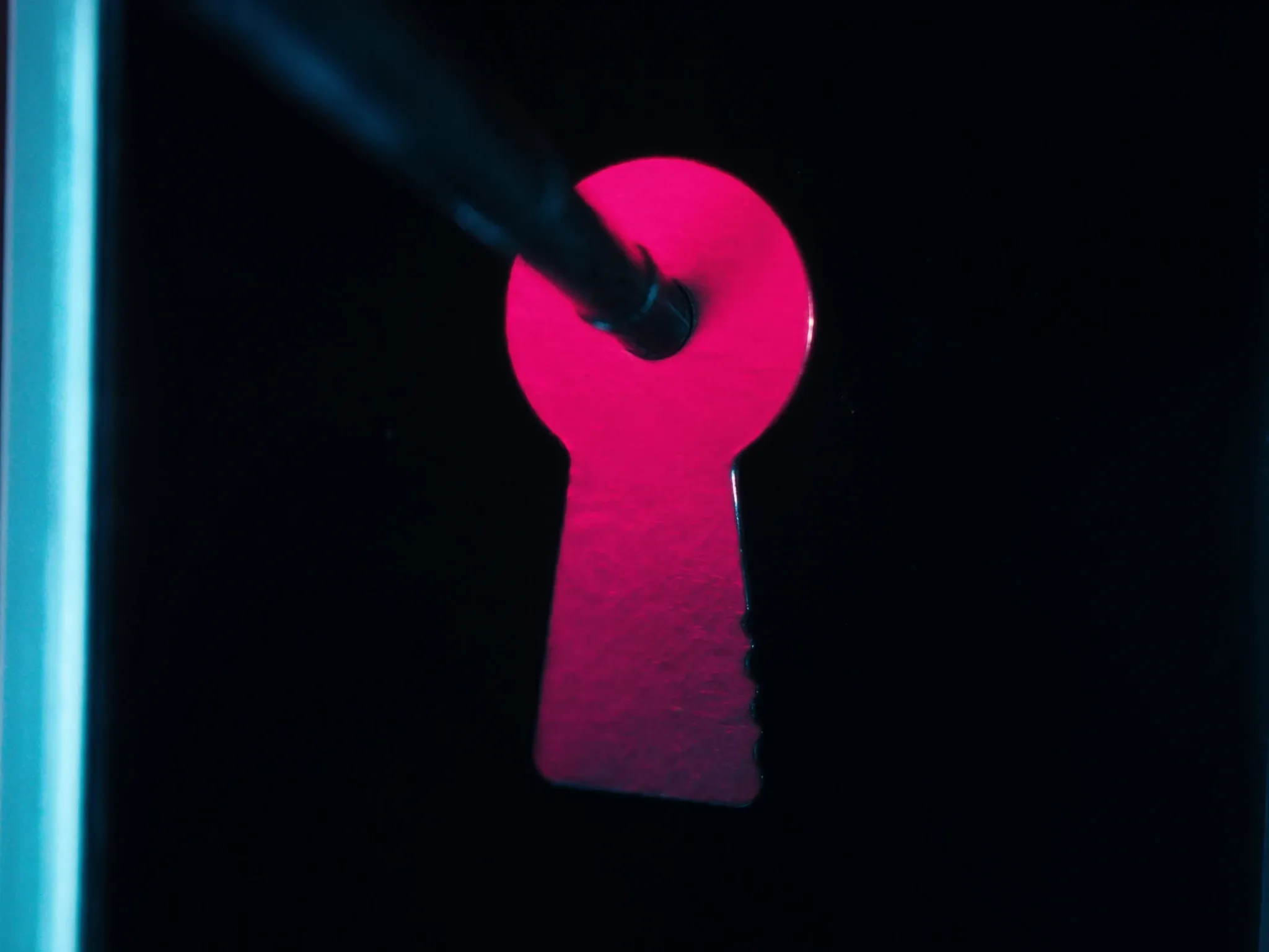 A standard key that doesn't fit a uniquely shaped lock, macro, pink light on dark metal