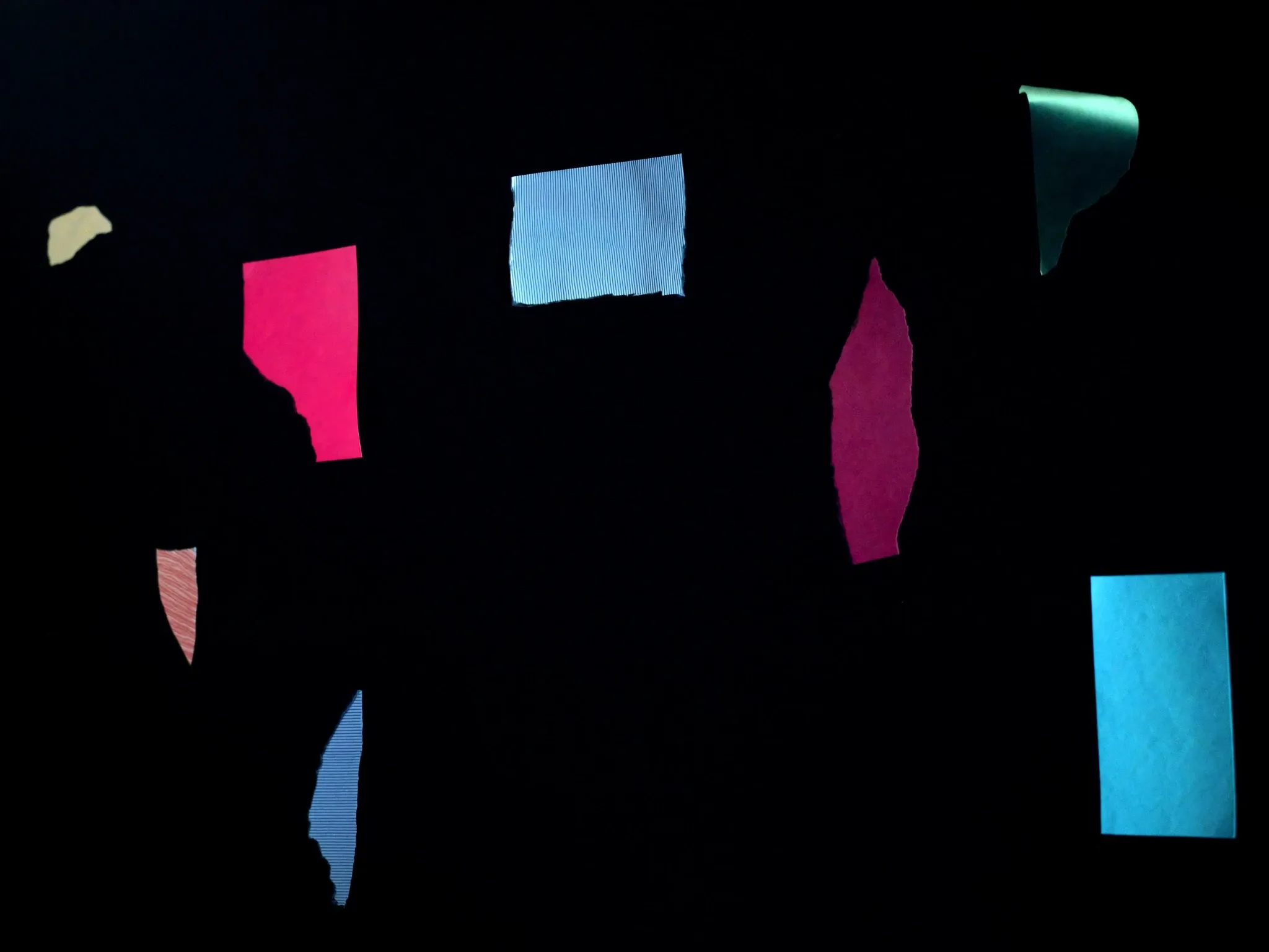 Mismatched paper offcuts in clashing colours and textures pinned unevenly to a dark board, hard side light, all blank