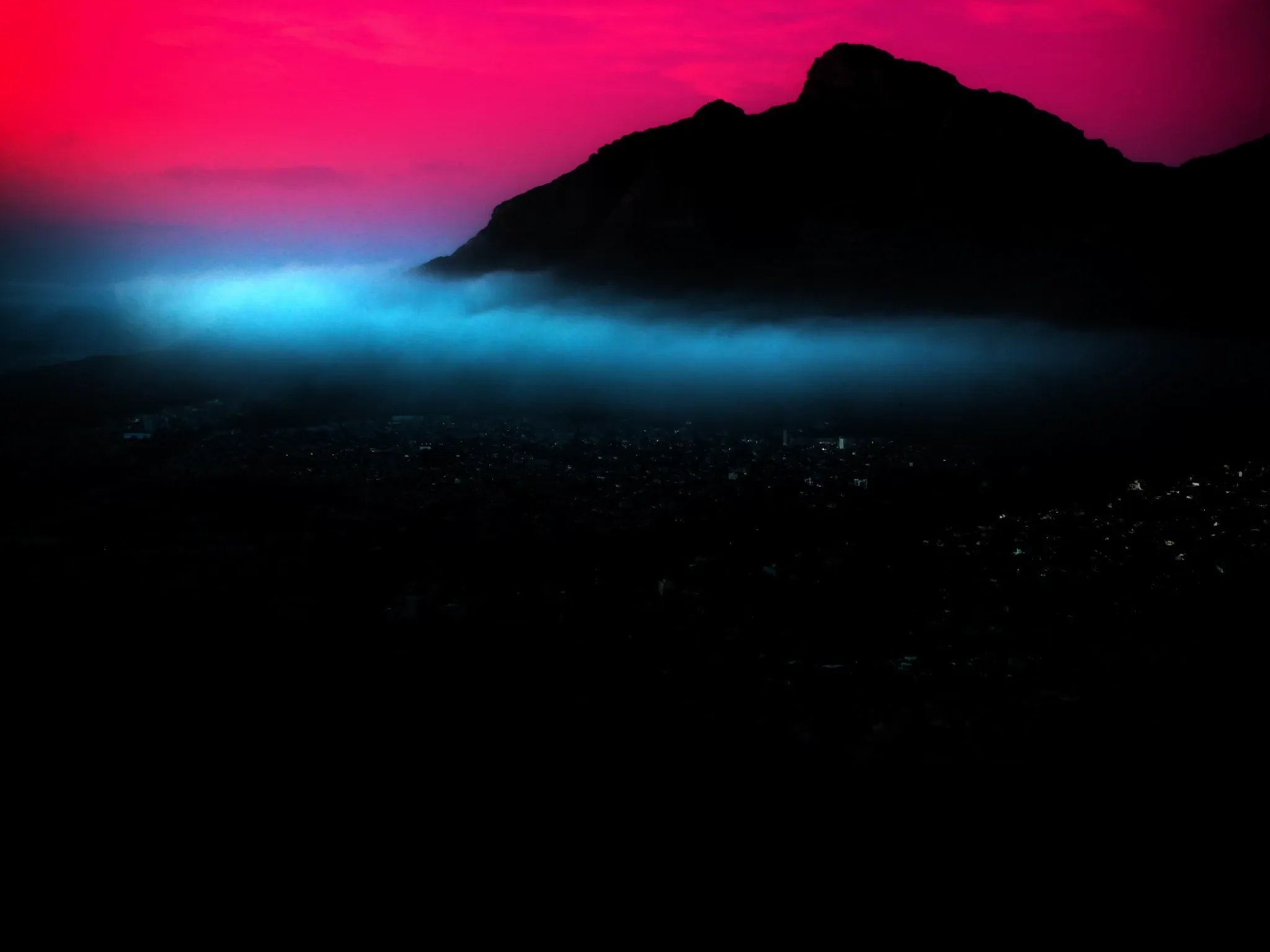 Thick fog rolling over Cape Town's city bowl at dusk seen from Signal Hill, the city lights below only faintly glowing through, Lion's Head rising above the fog