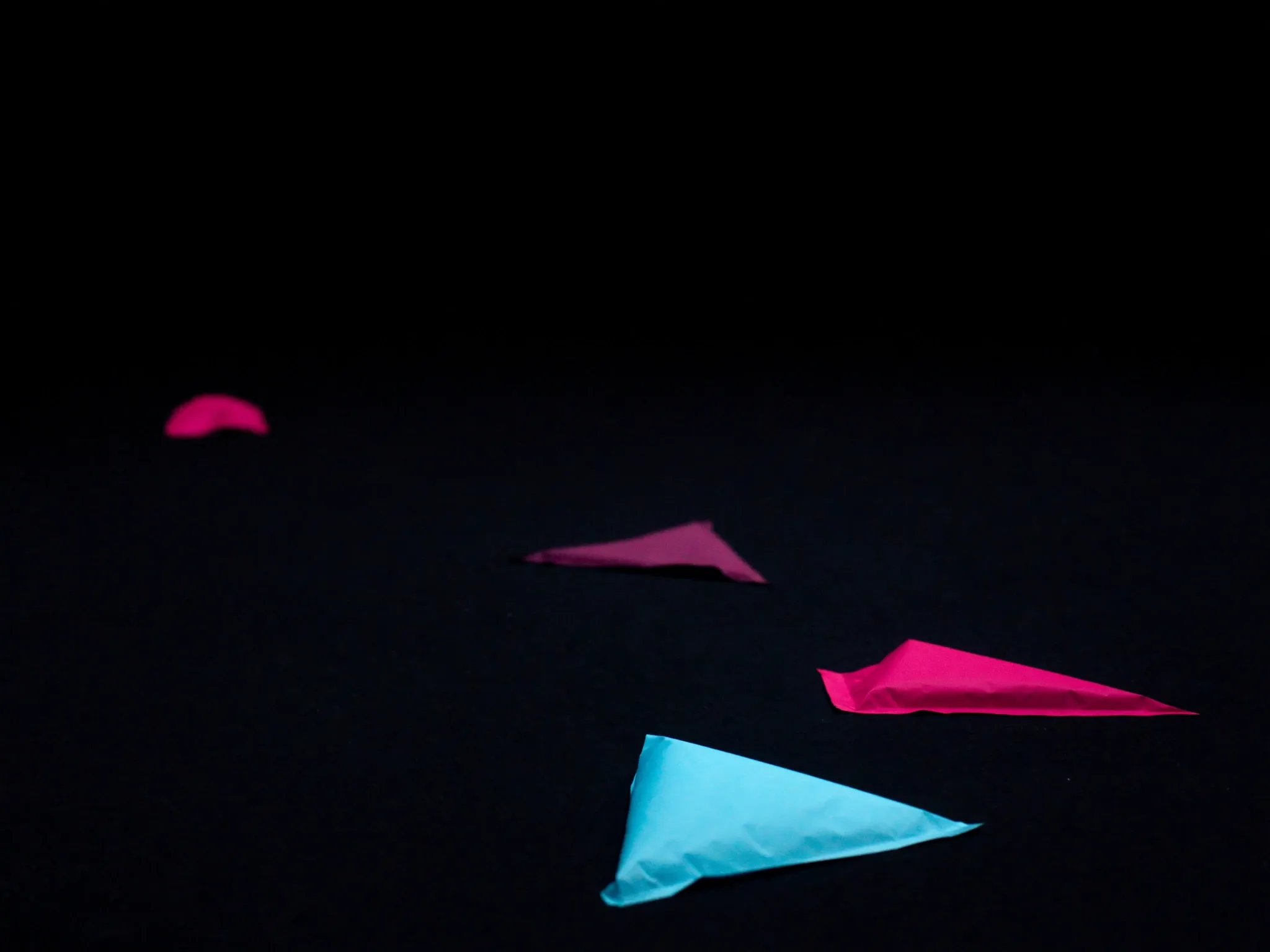 Small plain paper parcels scattered and abandoned across a dark floor, hard side light, no labels or lettering