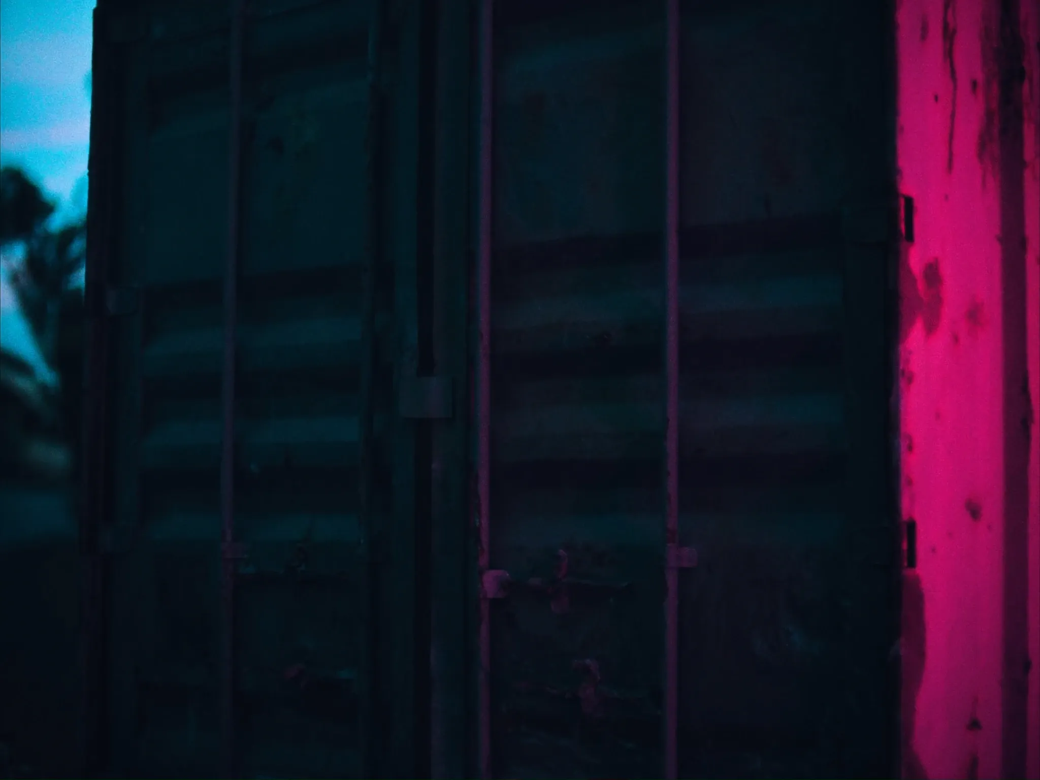 A weathered, rusted shipping container door in humid evening light, paint faded, close up, no lettering or numbers