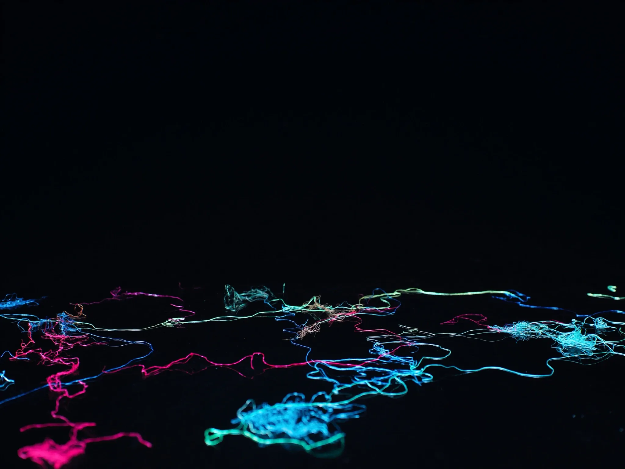 Loose threads in many colours spilling and tangling across a dark surface