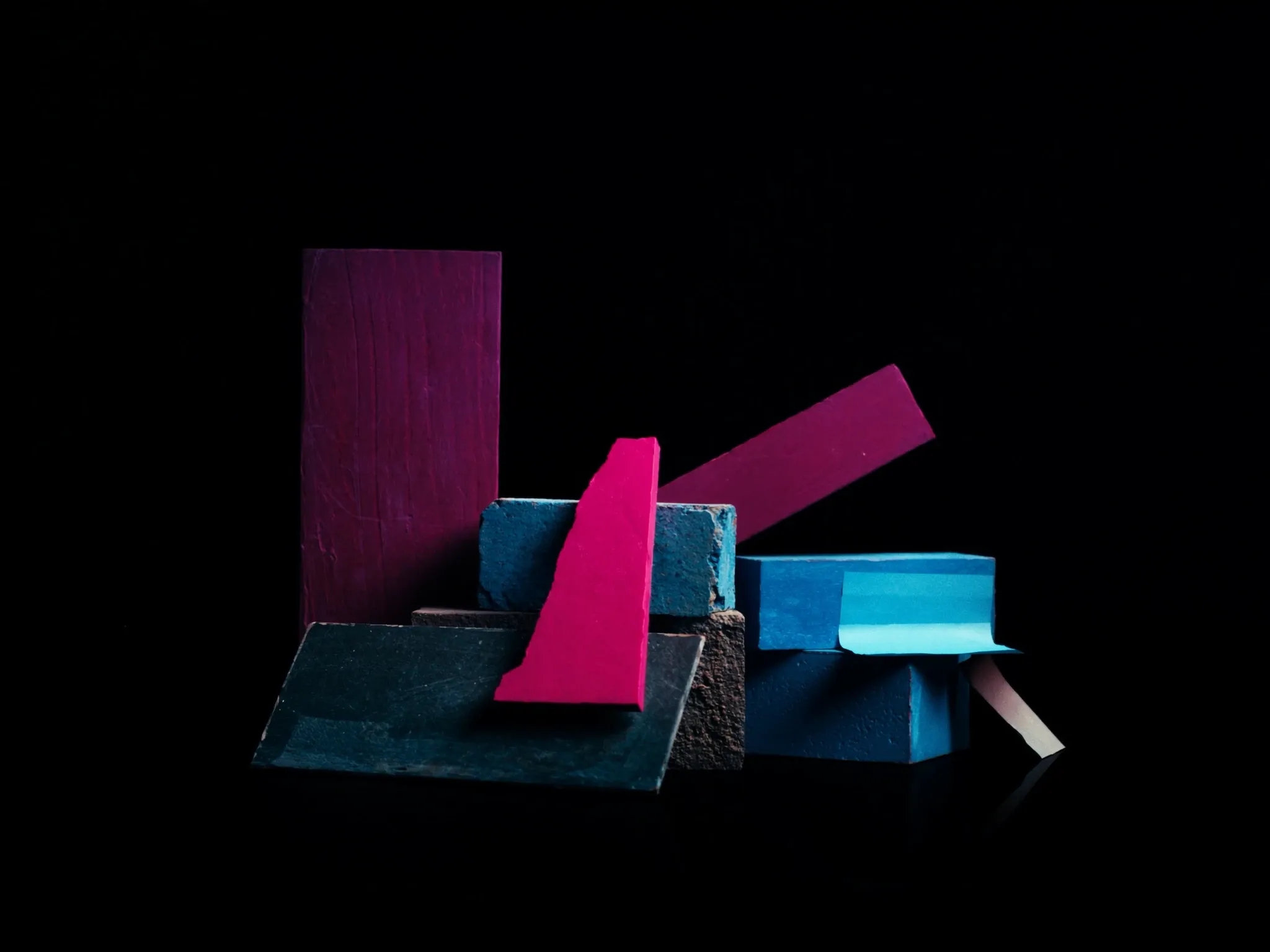 Mismatched building blocks of different materials stacked unevenly and leaning, lit dramatically against black