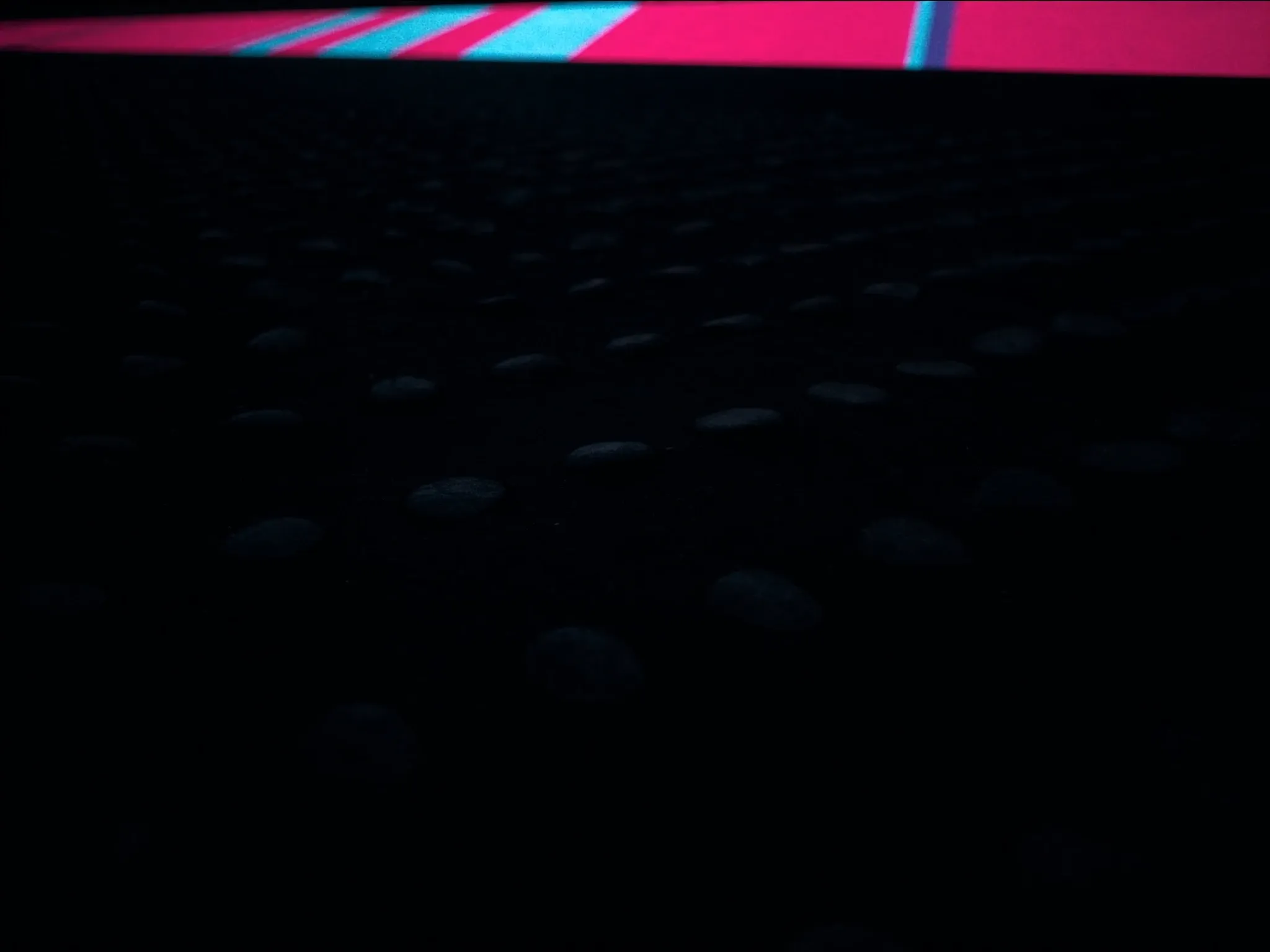 Rows of identical smooth black stones on dark sand under one dull, flat light, static and lifeless