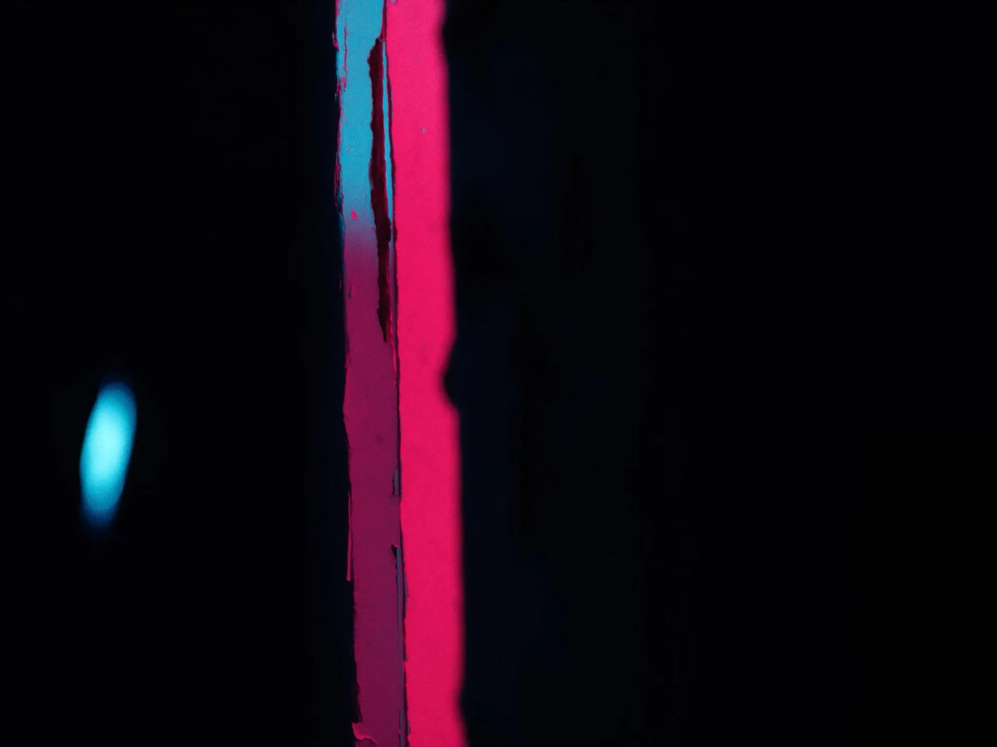 Layers of old peeling paint in mismatched colours on a weathered wall, close up, lit from the side in the dark