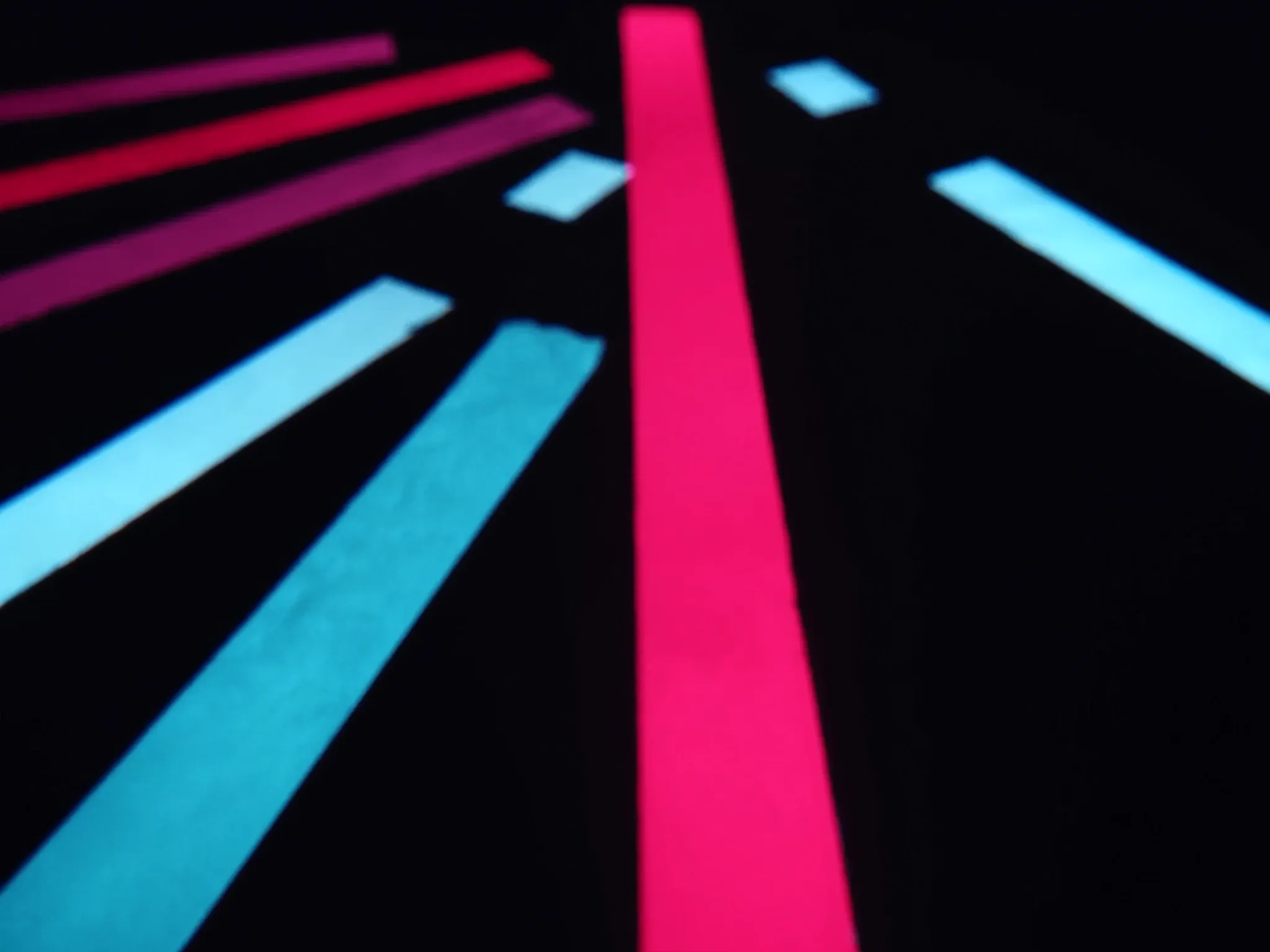 Several paths of light splitting from one point and running in different directions across a dark floor, pink and cyan