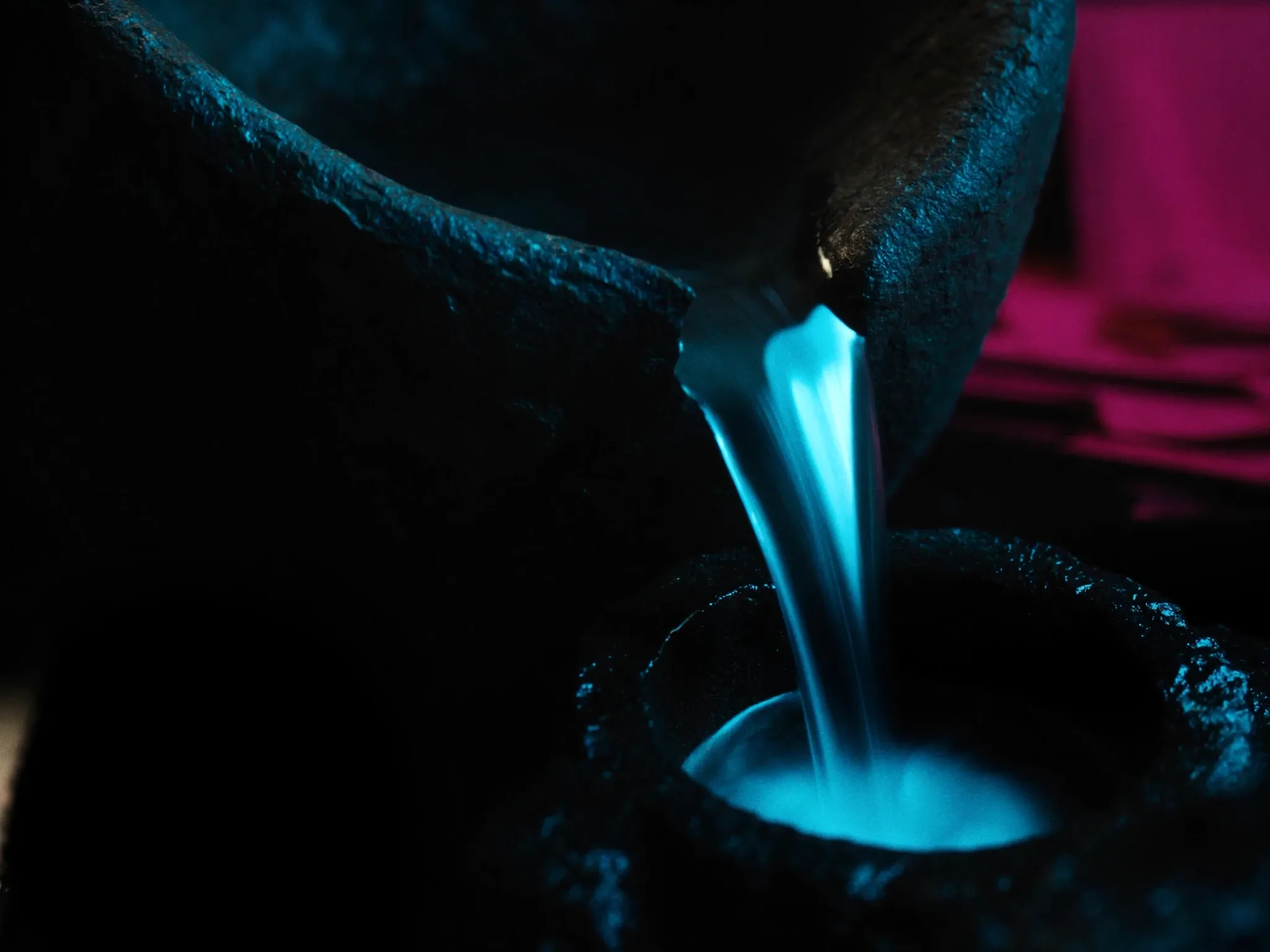 Water flowing from one stone basin into another, long exposure, smooth as glass, dark stone with cyan reflections