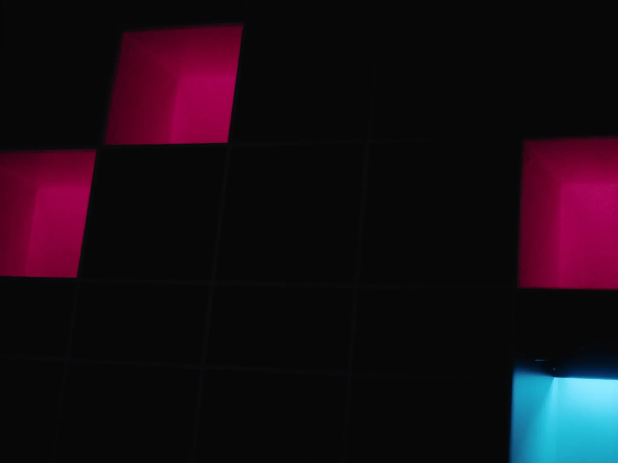 A wall of empty, perfectly ordered square cubby shelves in a dark room, a few compartments glowing pink and cyan from within, nothing inside them