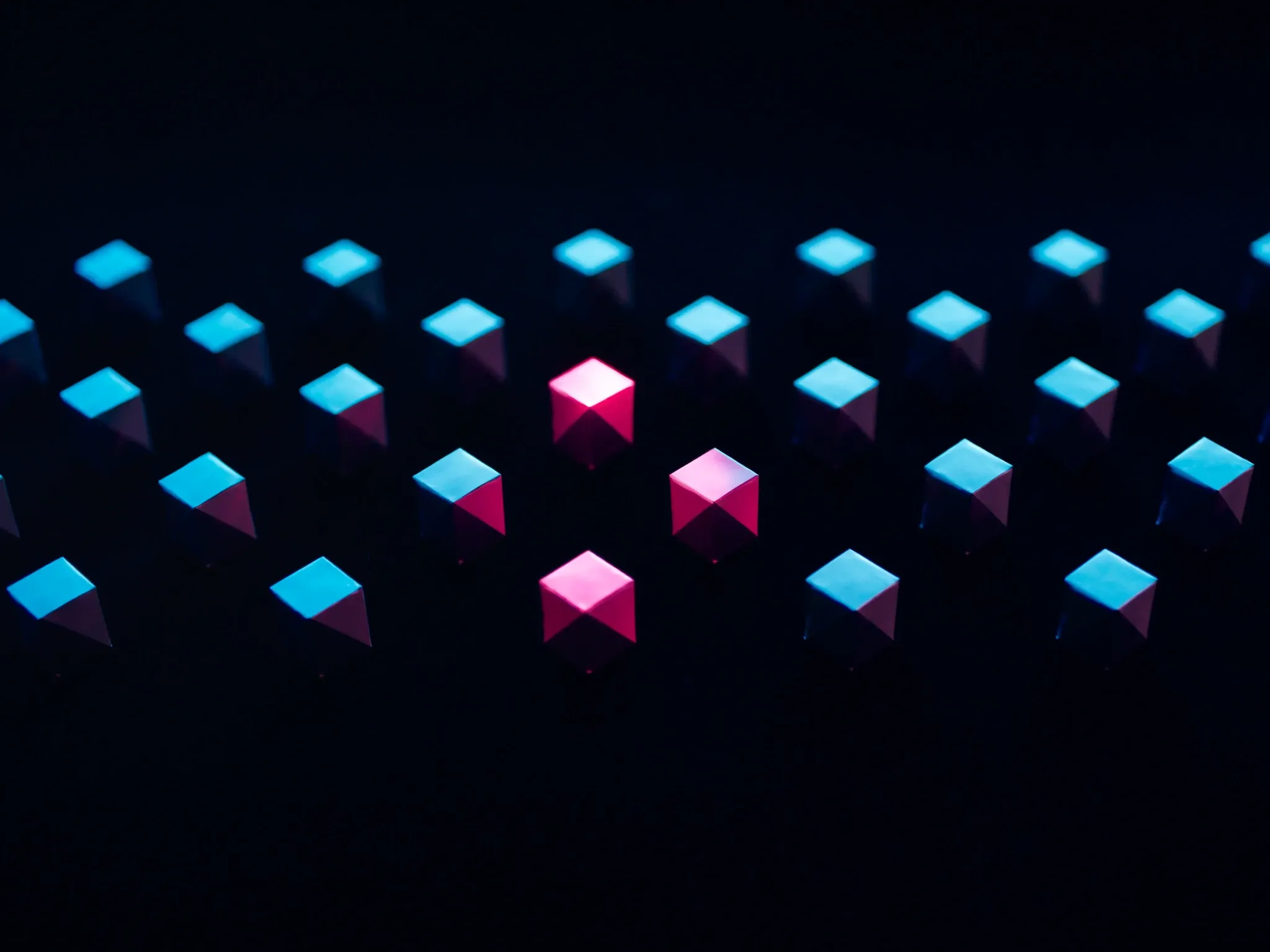 Rows of identical folded paper boxes in perfect alignment on a dark ground, one lit pink, studio light