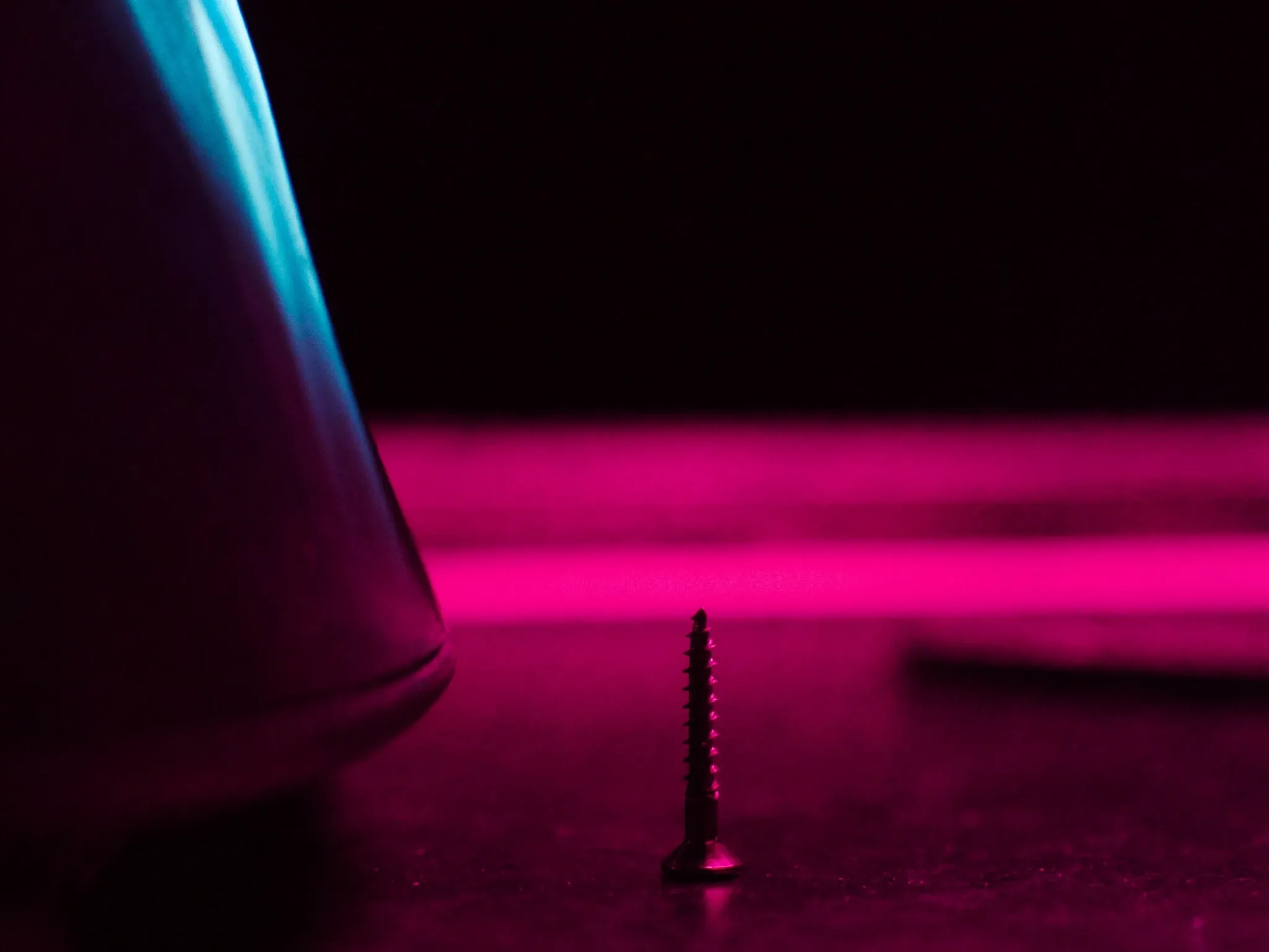 A single new brass bolt among old weathered ones on a dark steel plate, macro, soft pink light