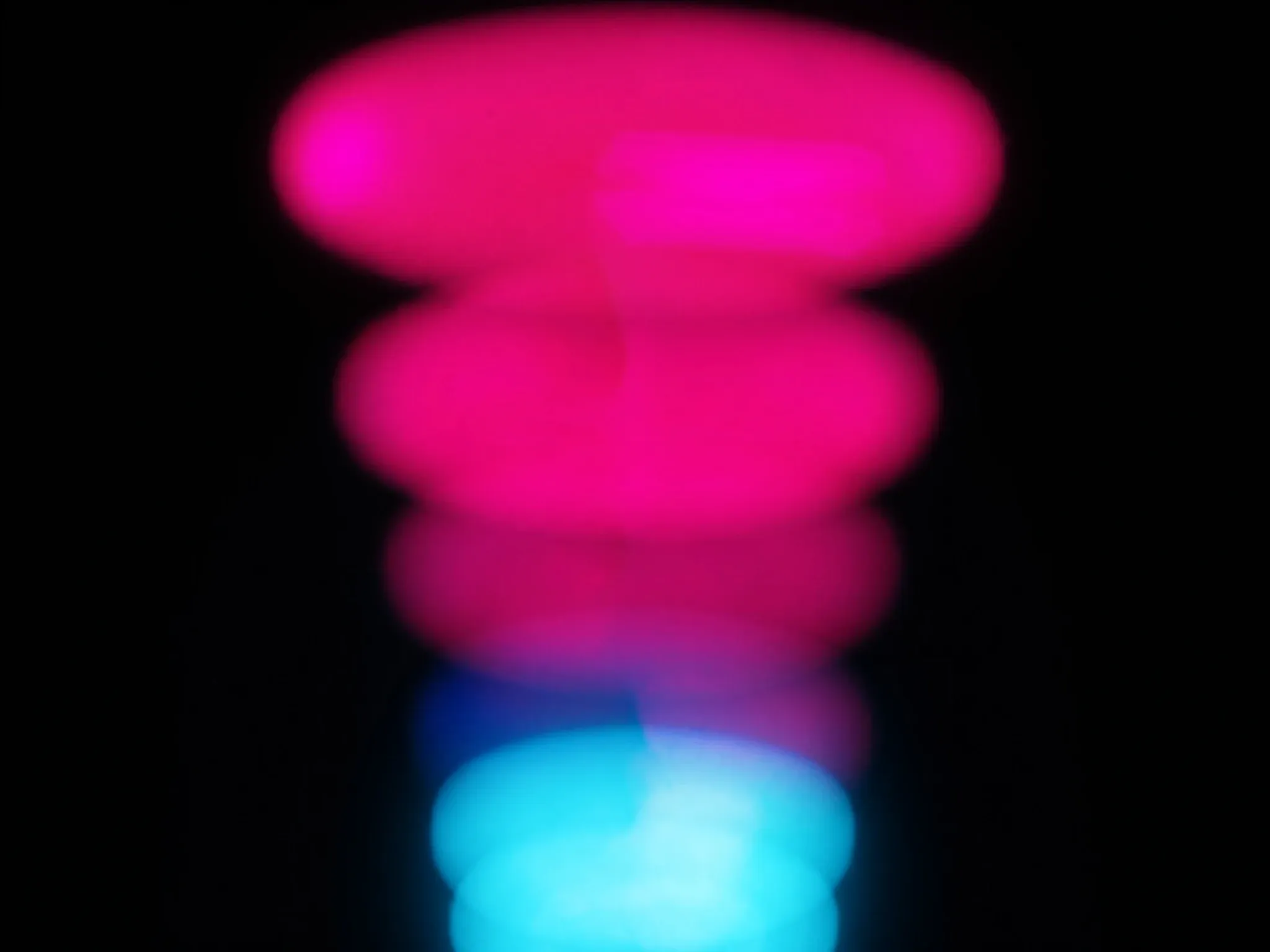 The same arc of light repeated several times in slightly different colours, pink, magenta and cyan, slow shutter, against black