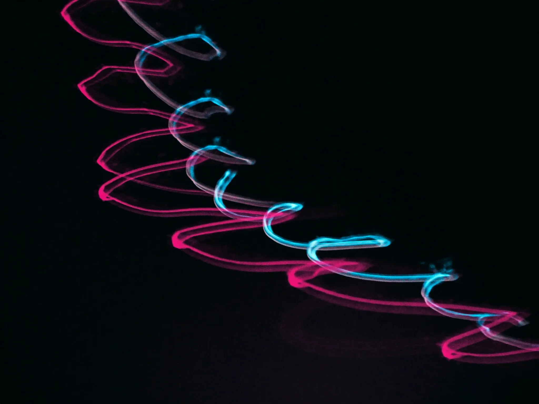 Long-exposure light tracing the same curve again and again through the dark, pink and cyan, like a repeated mark
