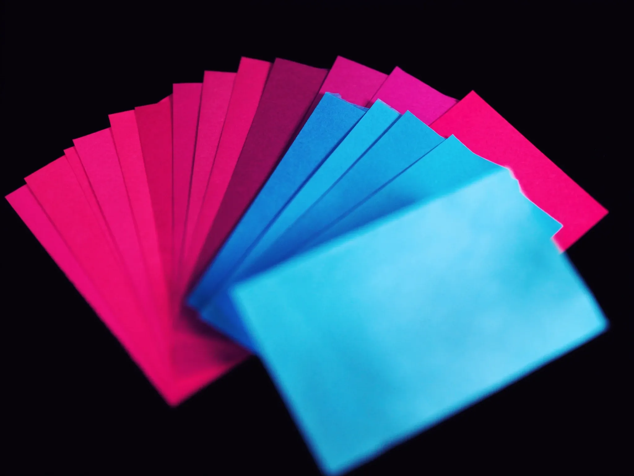 Sheets of coloured paper in a deliberate palette of magenta, pink, blue and cyan, fanned out in a precise arc on black