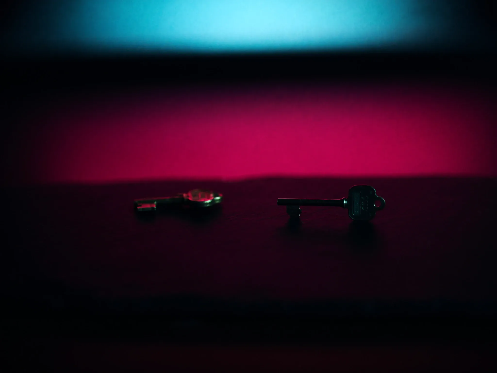 Two keys of different shapes lying side by side on black slate, one brass and one dark steel, soft pink and cyan light