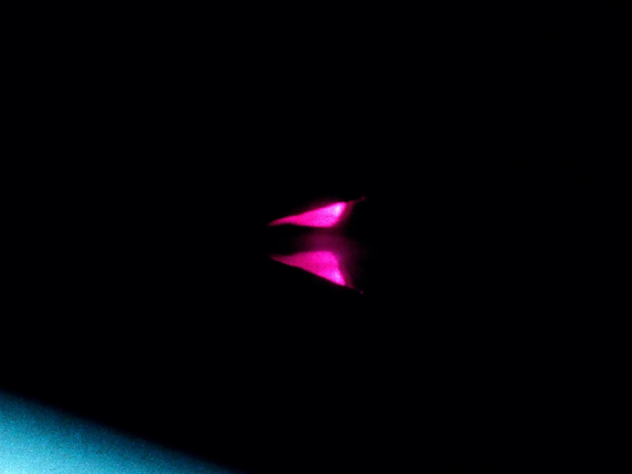 A tiny bright point of pink light and its exact reflection on a polished black surface, minimal, macro