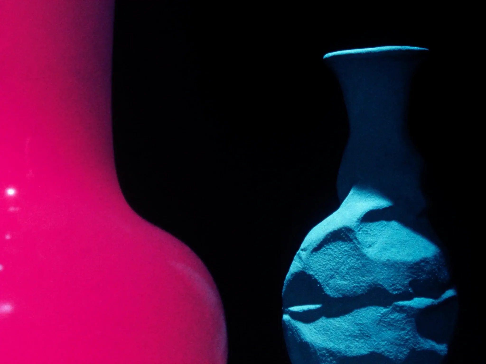 Two different stone vessels side by side, one smooth and polished, one textured and raw, lit pink and cyan against black