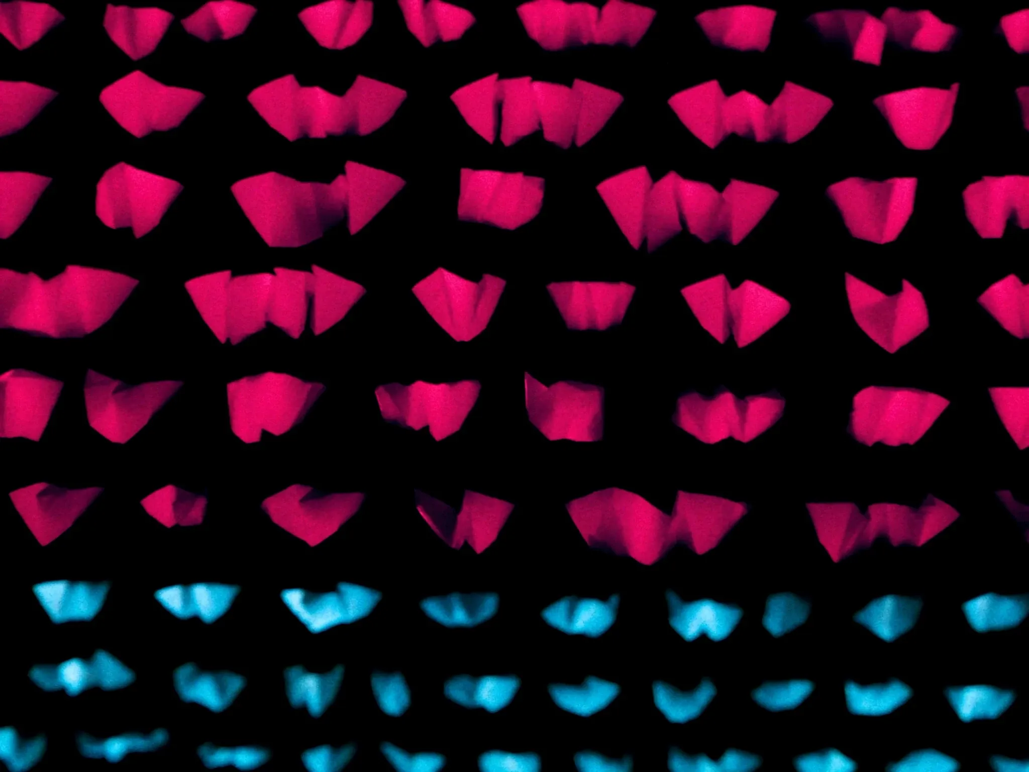 Rows of identical folded paper shapes in pink, lined up in perfect order on black, soft side light