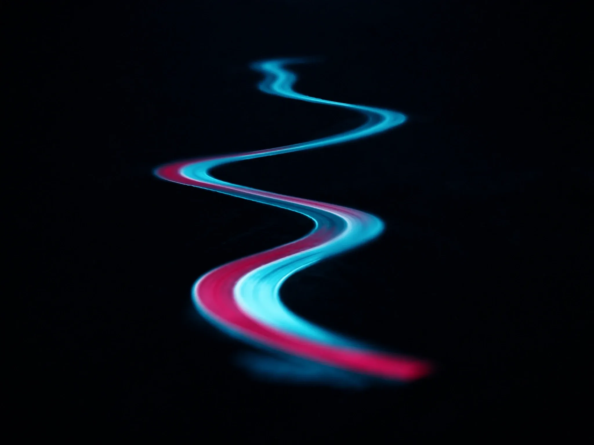 A winding mountain-pass road at night seen from high above, its centre line glowing faint cyan, guiding the way through the dark