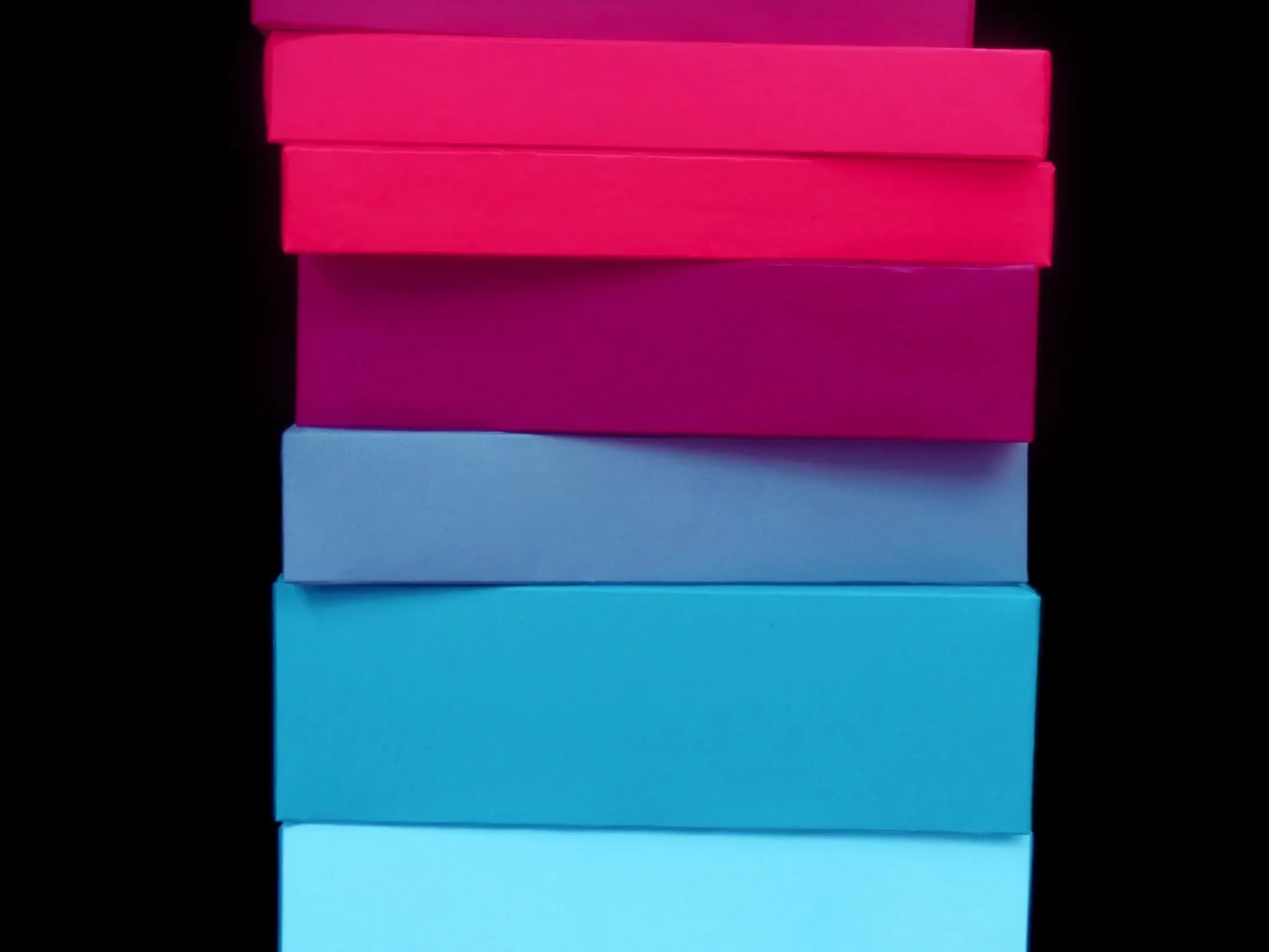 A neat stack of plain matte boxes in graduated pink and blue tones, crisp edges, studio light against black, no labels