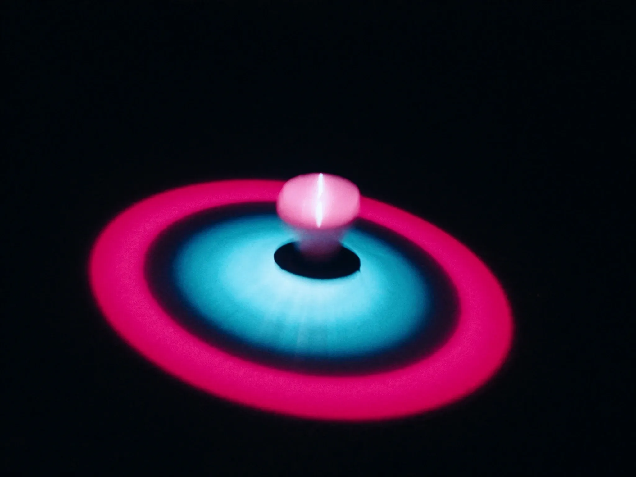 A spinning top casting a bright ring of pink and cyan light on a dark floor, motion blur
