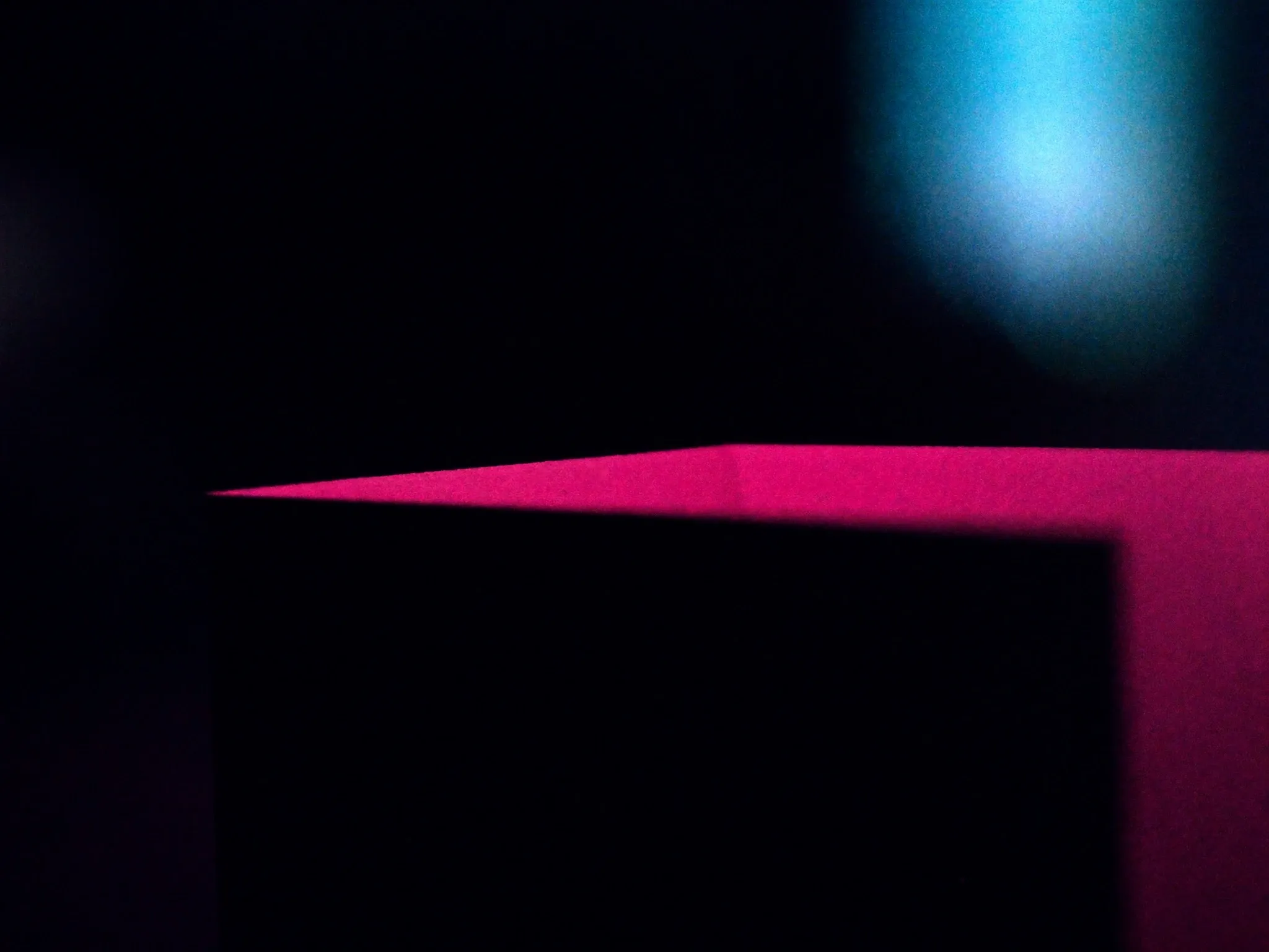 A single precise cut through a sheet of thick black card revealing a vivid pink layer beneath, macro, crisp edges