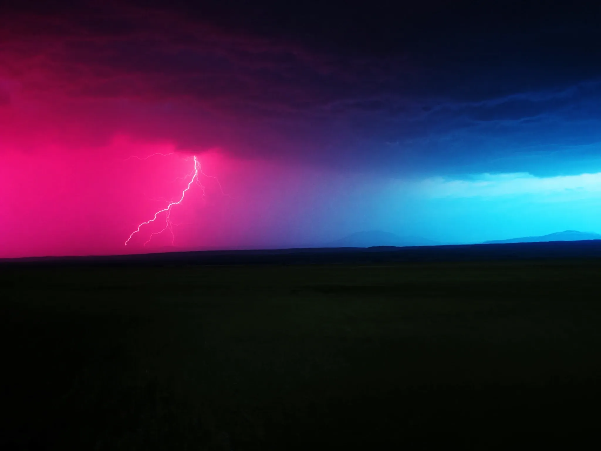 A highveld thunderstorm building over open grassland at dusk, one distant bolt of light, pink and deep blue sky