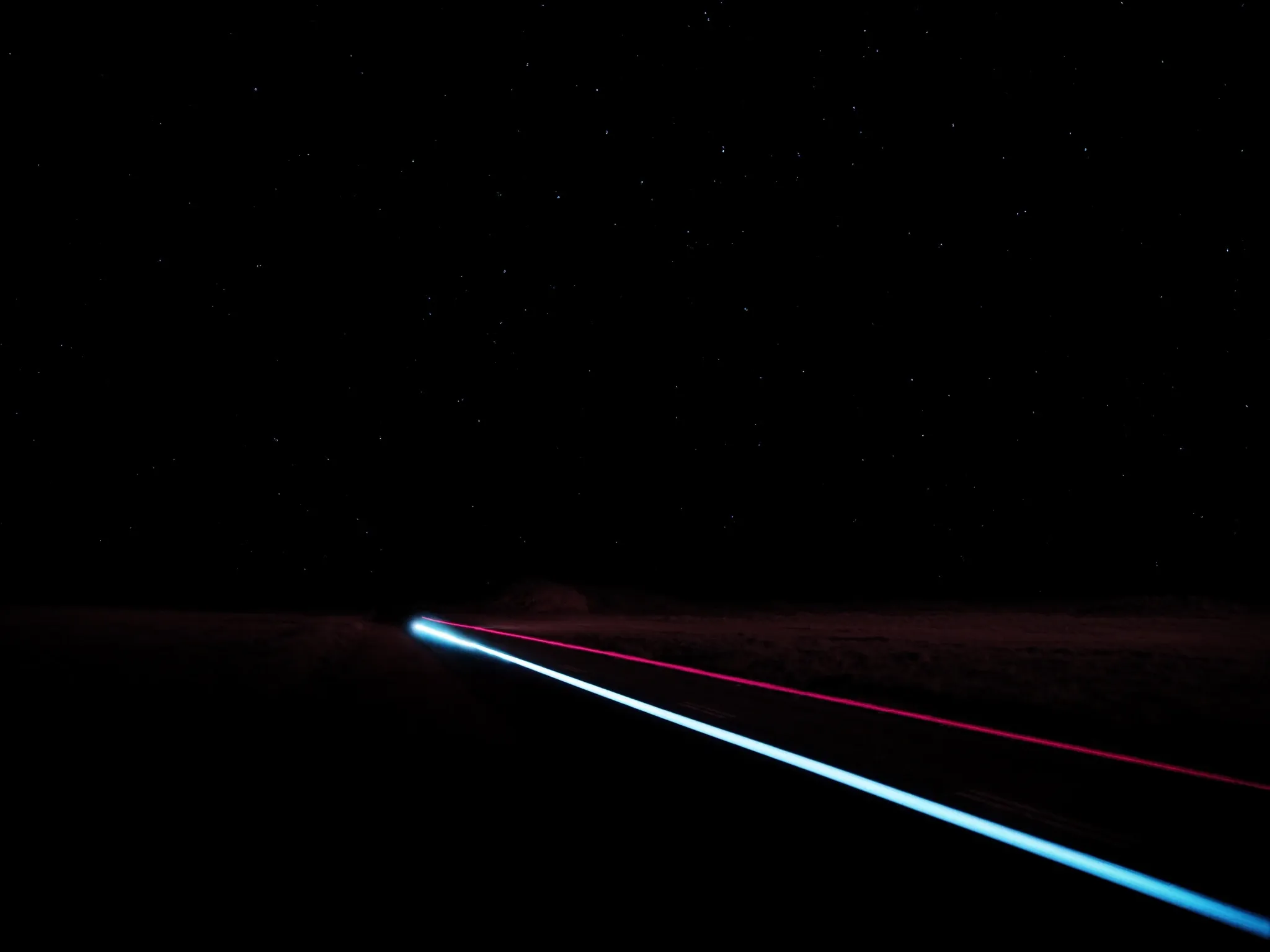 A single long-exposure light trail travelling along a lone road through the Karoo at night, a sky full of stars above