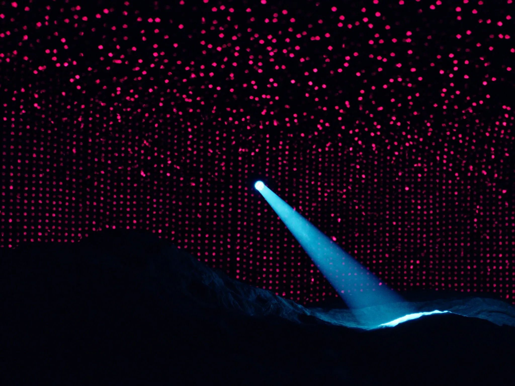 A single narrow beam of light picking out one point within a dense field of small glowing dots