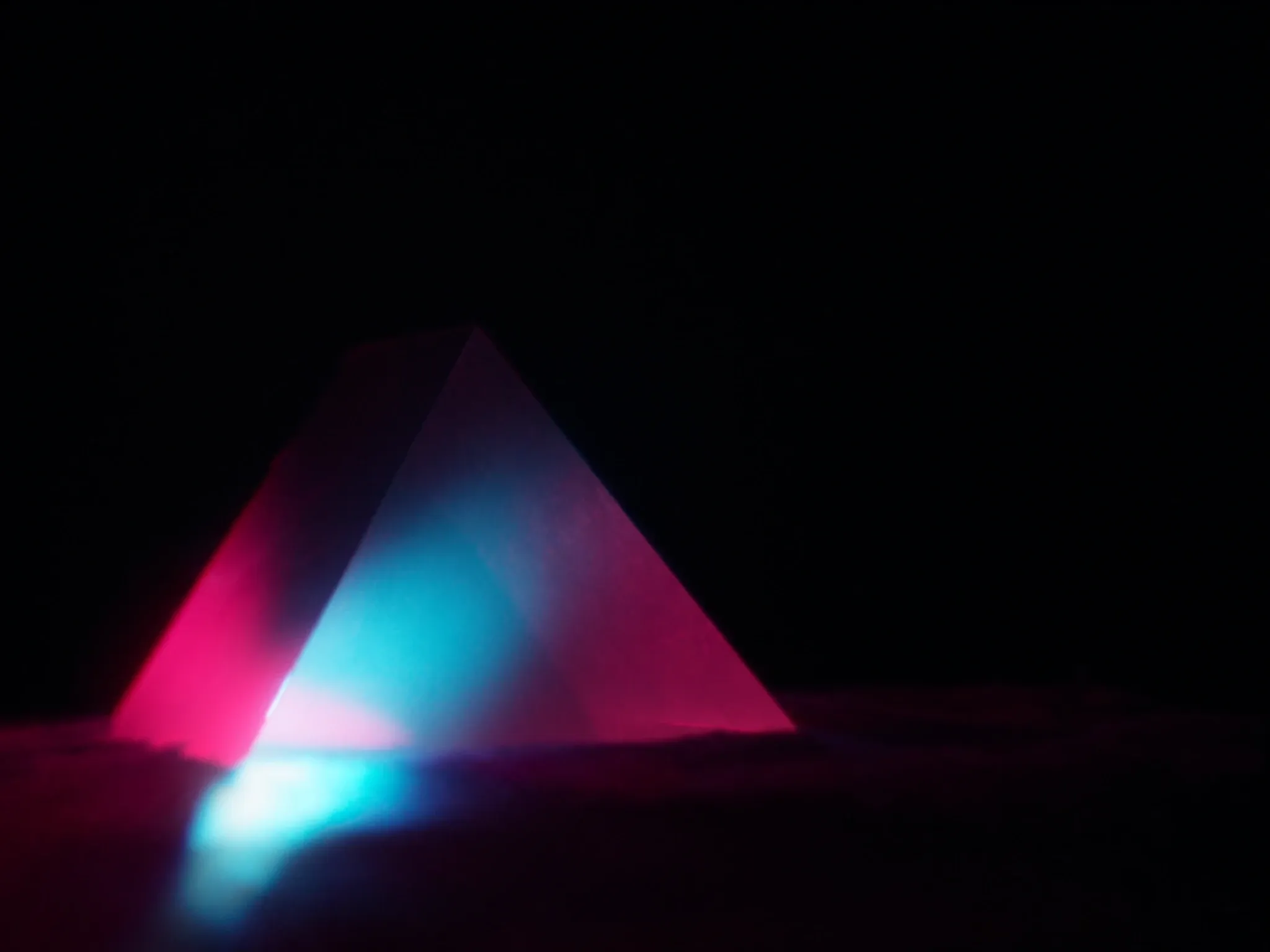 Light refracting through a glass prism into a fan of pink and blue across dark velvet