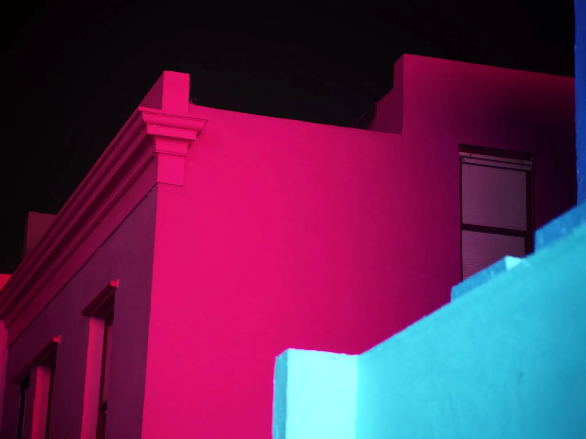 Close abstract crop of Bo-Kaap house walls in Cape Town: flat planes of pink and turquoise paint meeting at clean angles, hard evening light and long shadows, no doors or signs