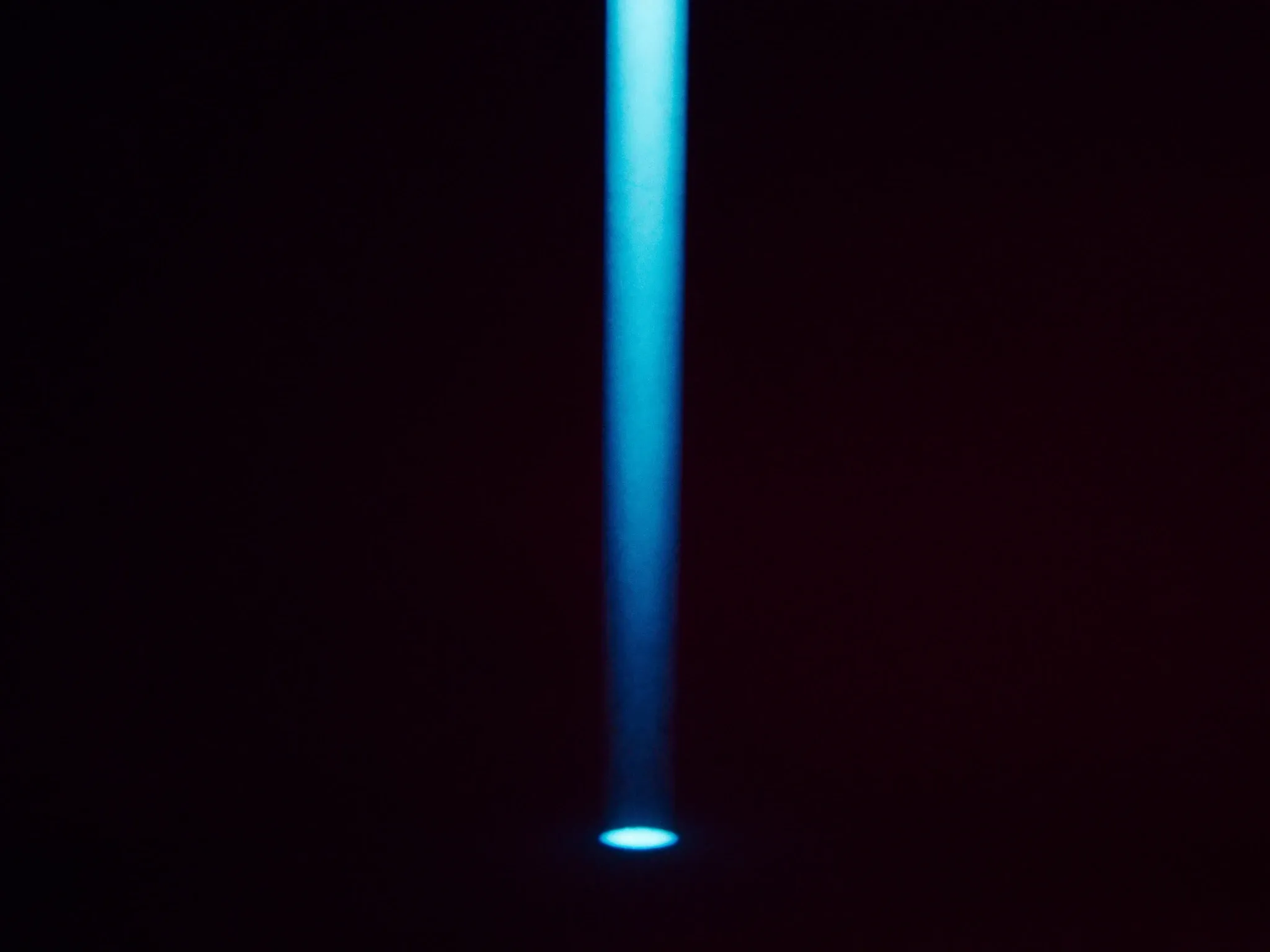 A narrow beam of light through haze landing exactly on one small glowing point in the dark