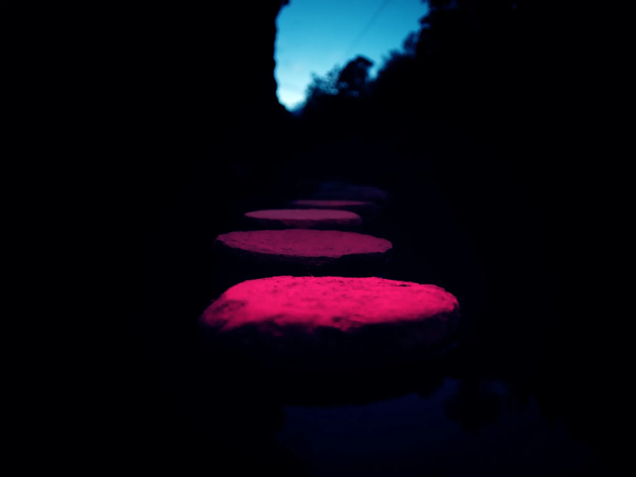 Stepping stones crossing still dark water toward a soft light, blue hour