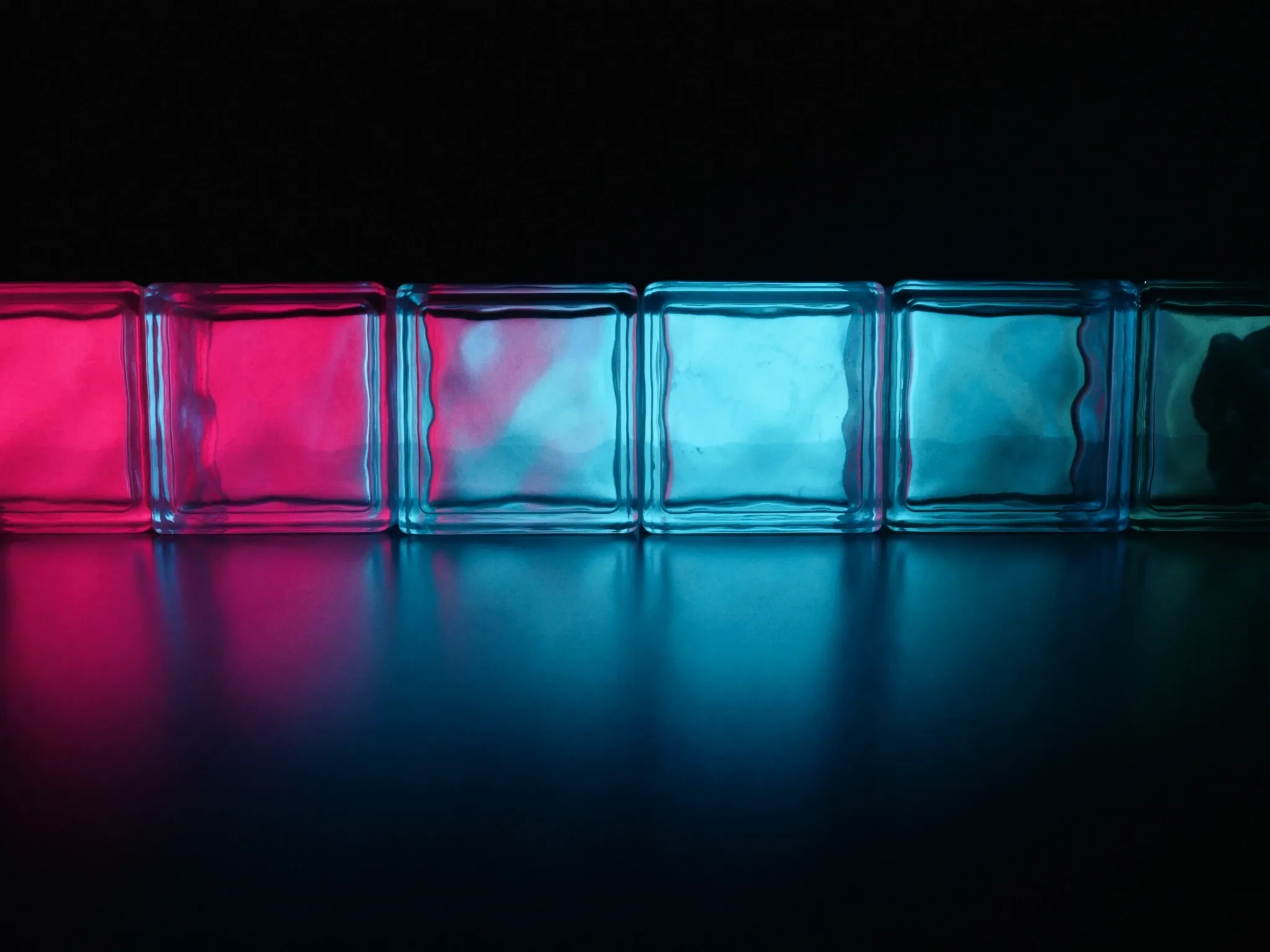 Light passing through a row of clear glass blocks in perfect alignment, cyan and pink refractions on a dark surface