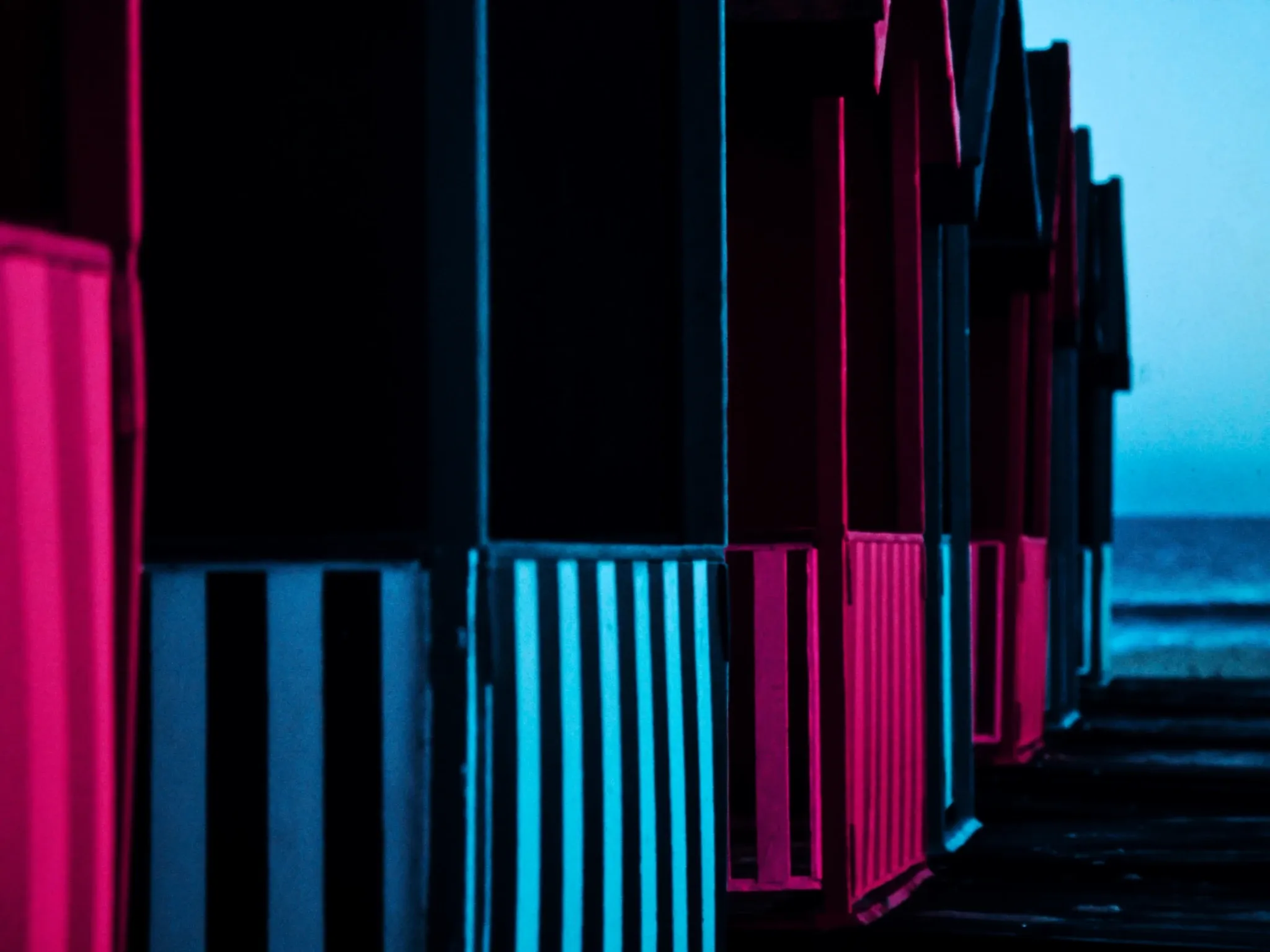 The row of brightly painted Victorian wooden bathing boxes on the beach at St James, Cape Town, in early morning light: bold stripes of colour, calm sea behind, no signage