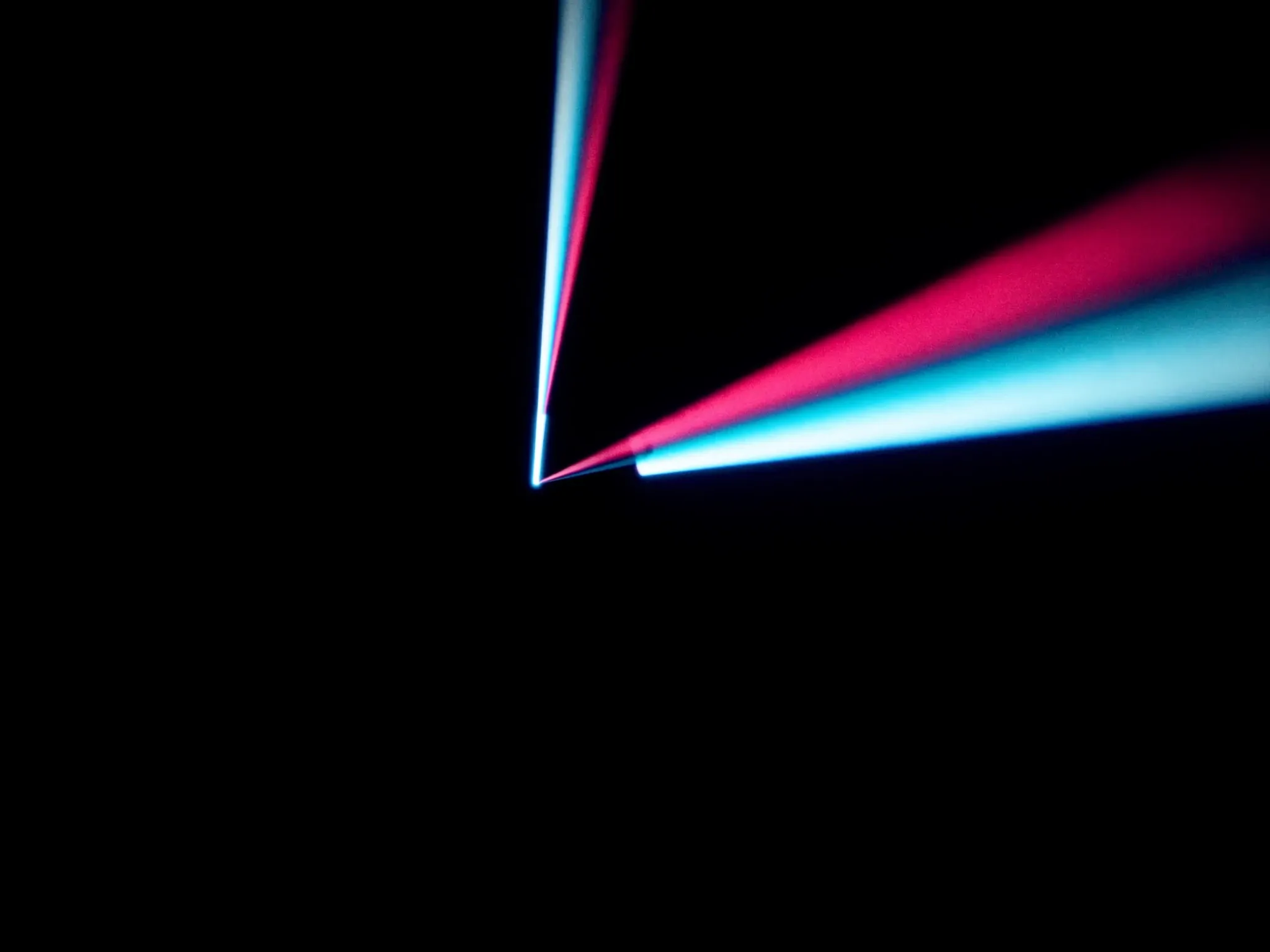 A glass prism splitting one white beam into pink and cyan rays, against black